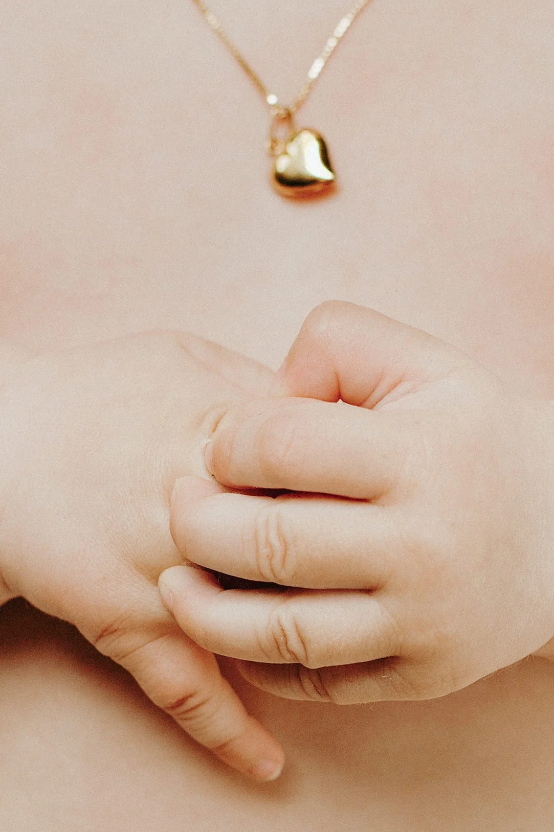 Babyfotografering- Nærbilde av hender og gullsmykke formet som et hjerte.