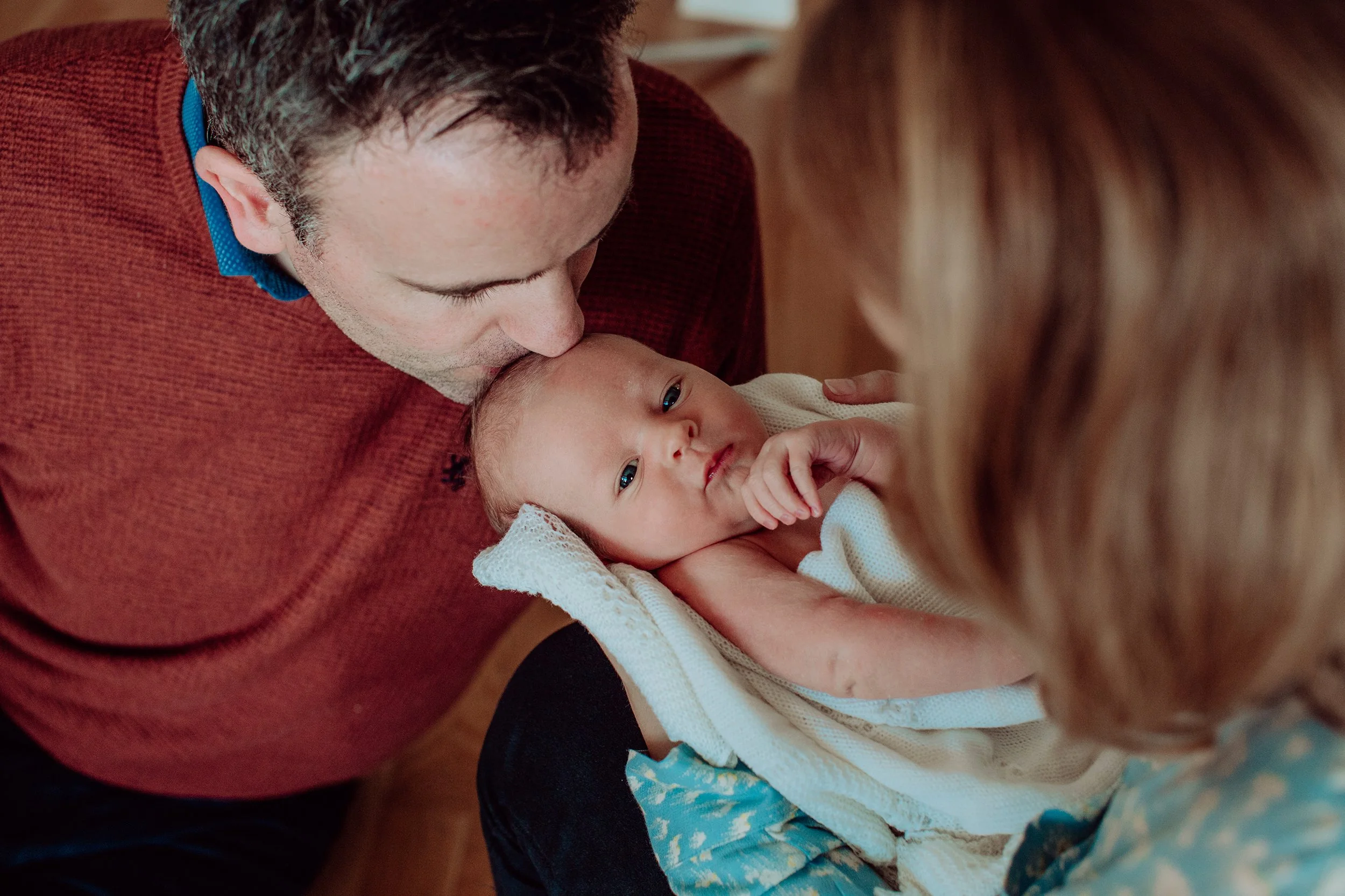 Mor og far sammen med baby på nyfødtfotografering hjemme.
