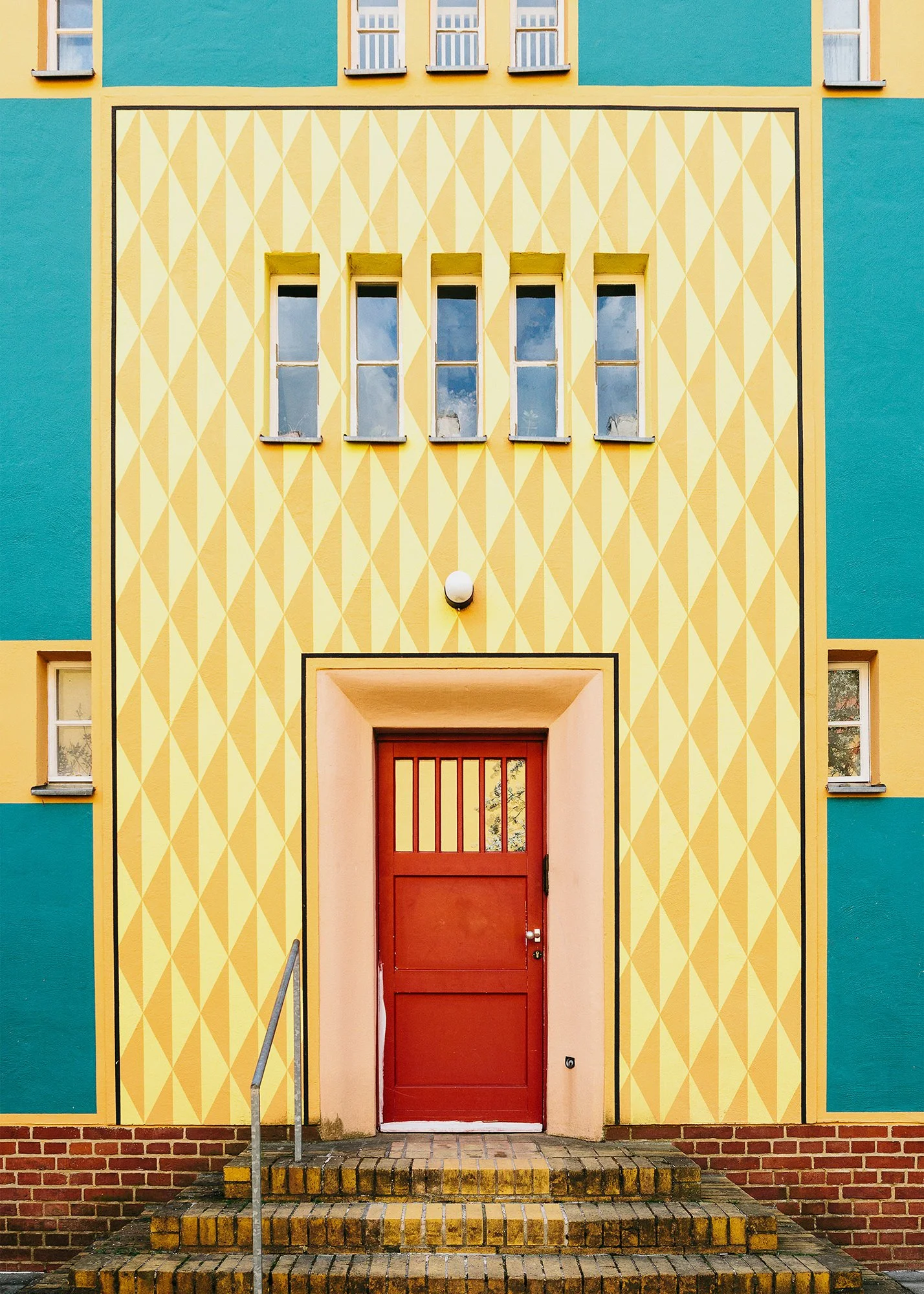 Fargerikt inngangsparti med gul og turkis vegg og rød dør i boligfeltet Gartenstadt Falkenberg i Berlin, tegnet av arkitekt Bruno Taut.