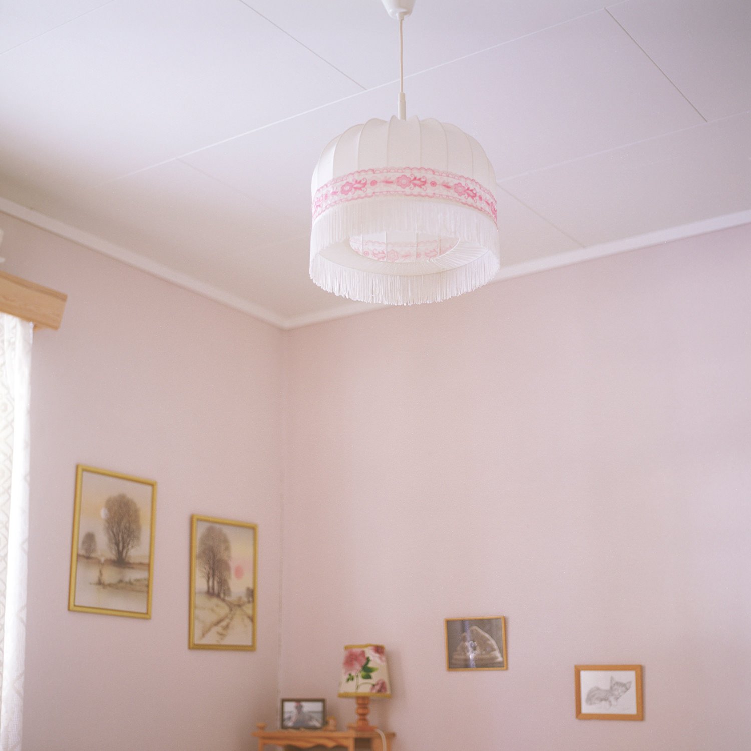 Utsnitt av soverom med rosa vegger og hvit taklampe med frynser.