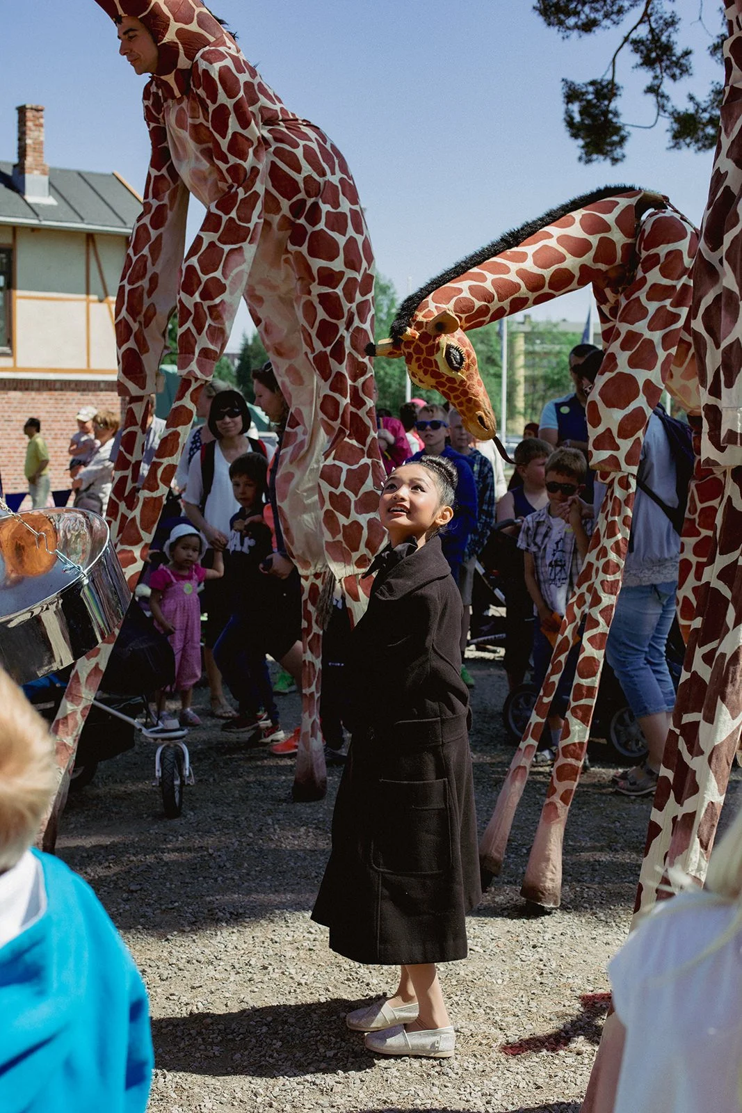 Stoppested Verden internasjonal barnefestival. Forbauset jente stirrer opp mot artister i giraffdrakter på stylter.