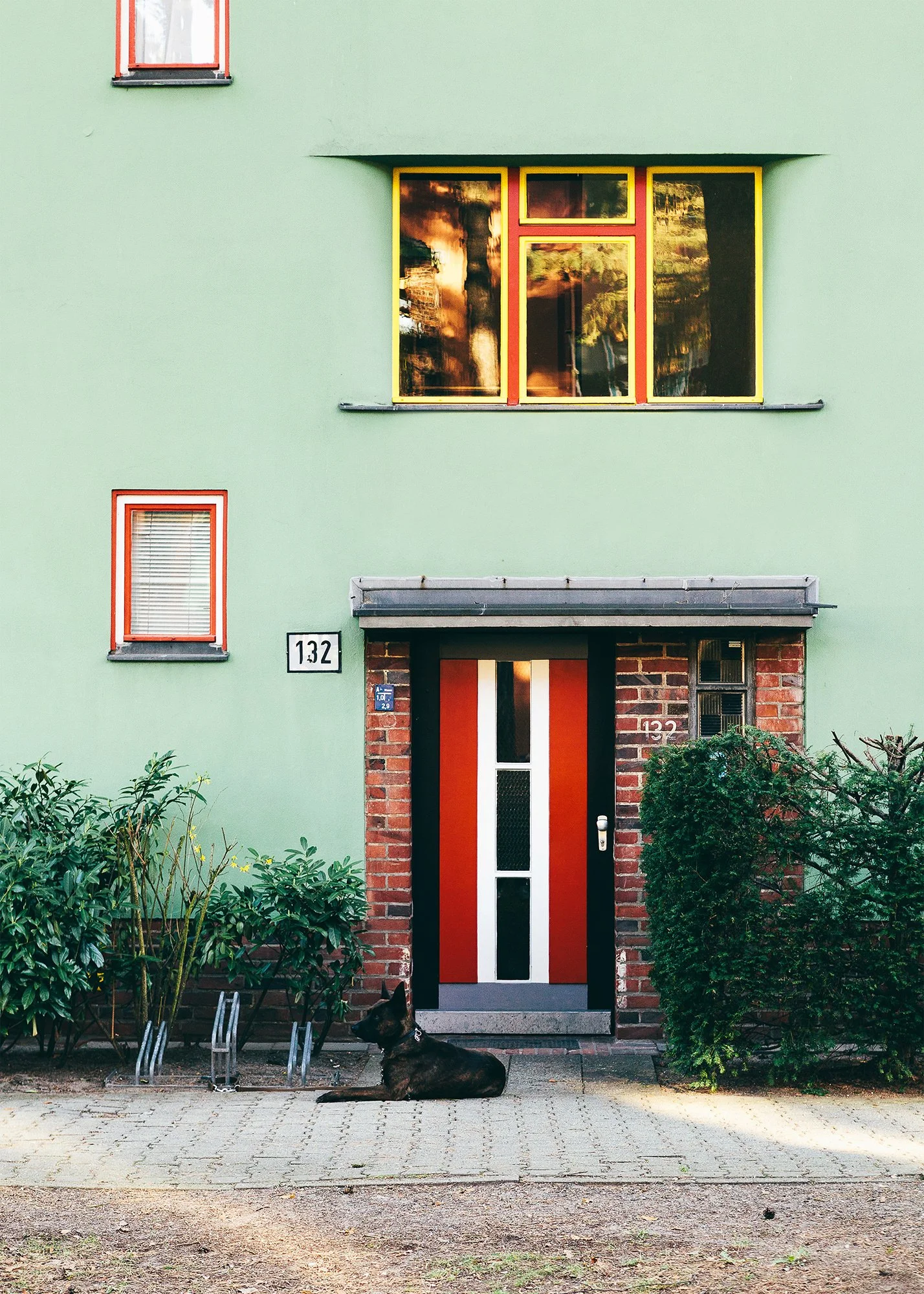 Boligfelt i Onkel Toms Hütte i Berlin, tegnet av arkitekt Bruno Taut. Grønnmalt boligblokk med rød inngangsdør. En hund ligger utenfor.