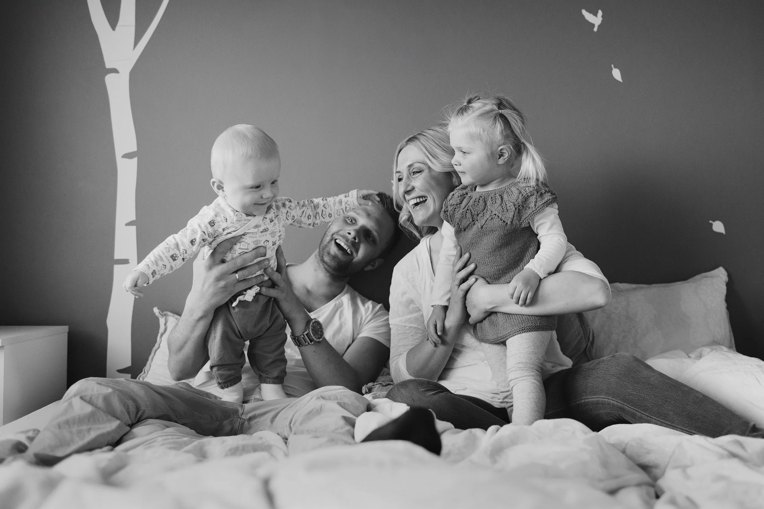 Familiefotografering innendørs i naturlig lys. Familie på fire med to små barn leker sammen.