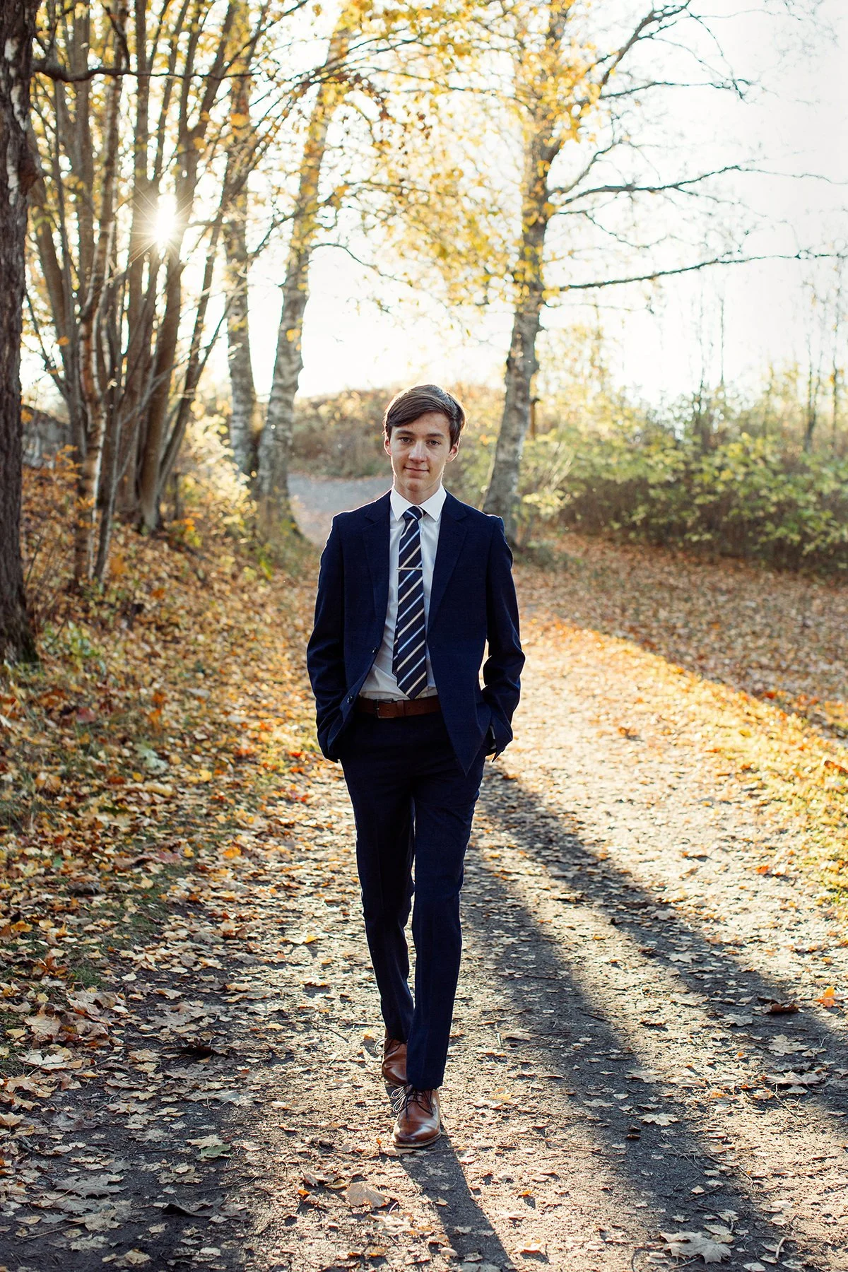 Konfirmantfotografering av gutt gående mot kamera på en sti i dress