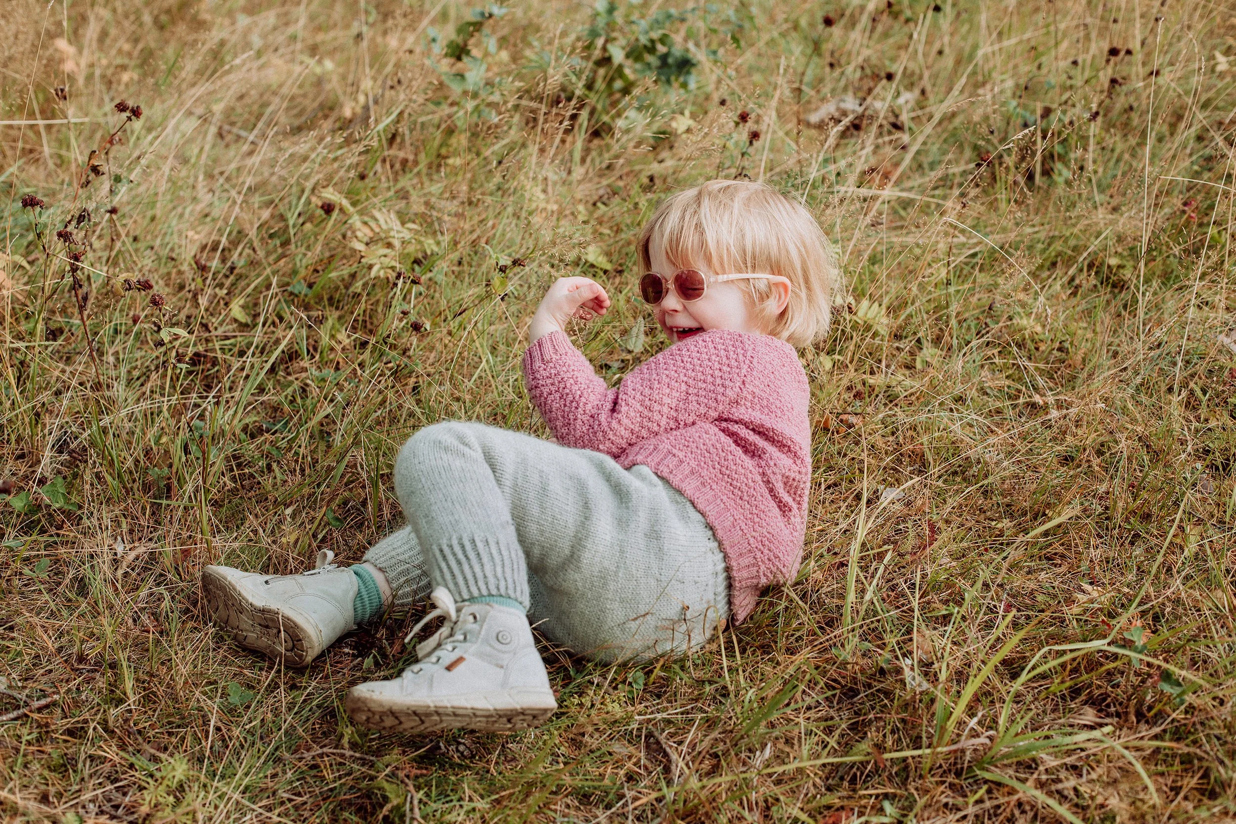Et barn ligger på bakken i gresset og ler