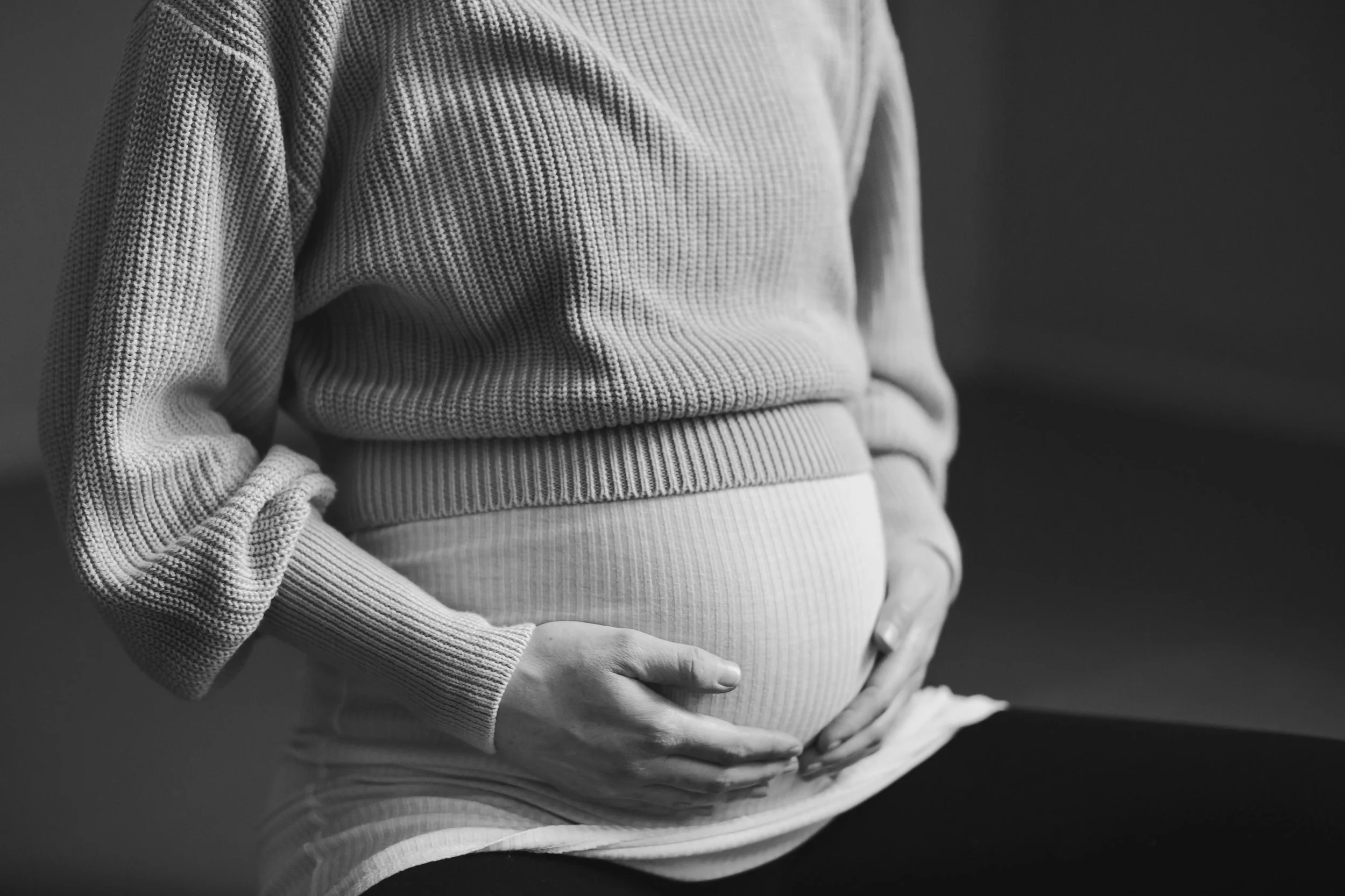 Gravid kvinne holder hendene på magen mens hun sitter avslappet på gulvet.