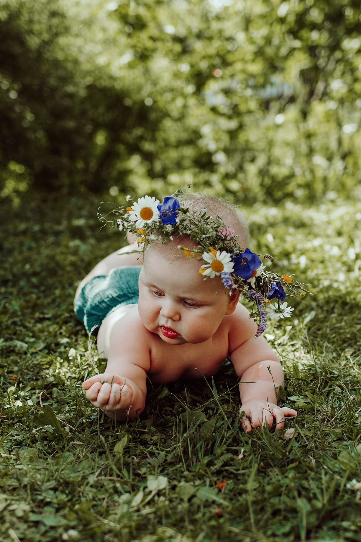Babyfotografering av halvt år gammel baby liggende på gresset med blomsterkrans.