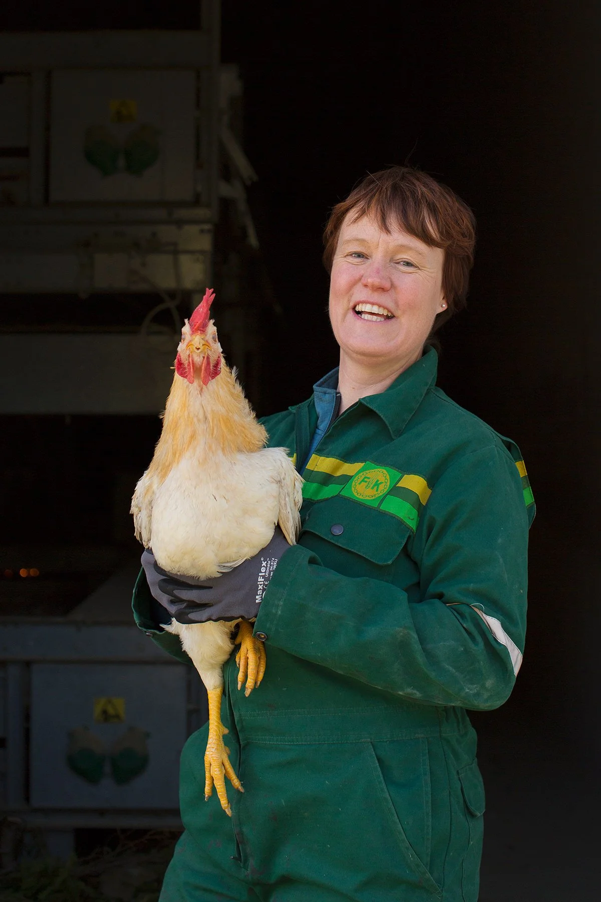 Kvinnelig bonde i drakt fra Felleskjøpet smiler mens hun holder en hane i armene.