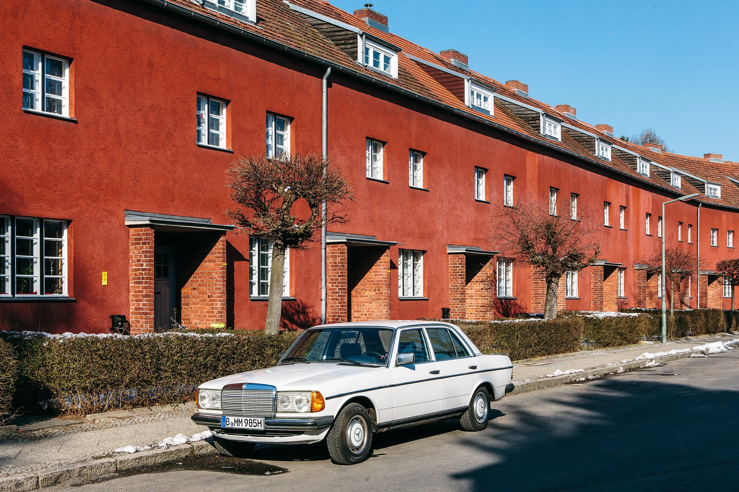 Bolighus i rød mur med rekkehus bortover gaten i området Hufeisensiedlung i Berlin.