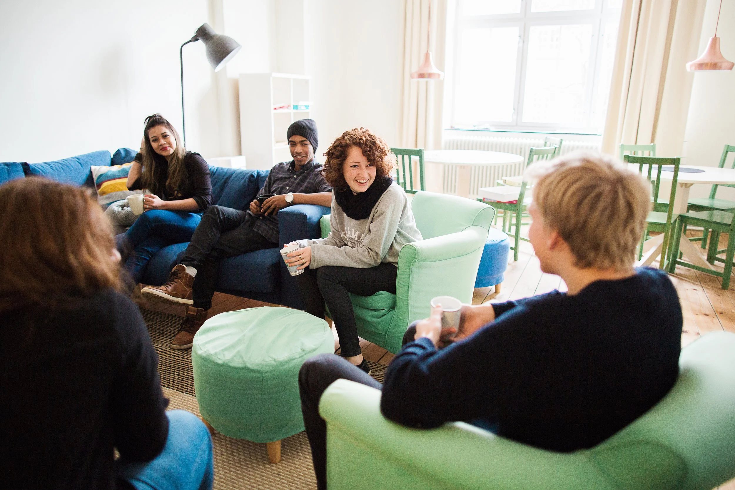 Fem studenter sitter i oppholdsrommet og snakker og ler sammen.