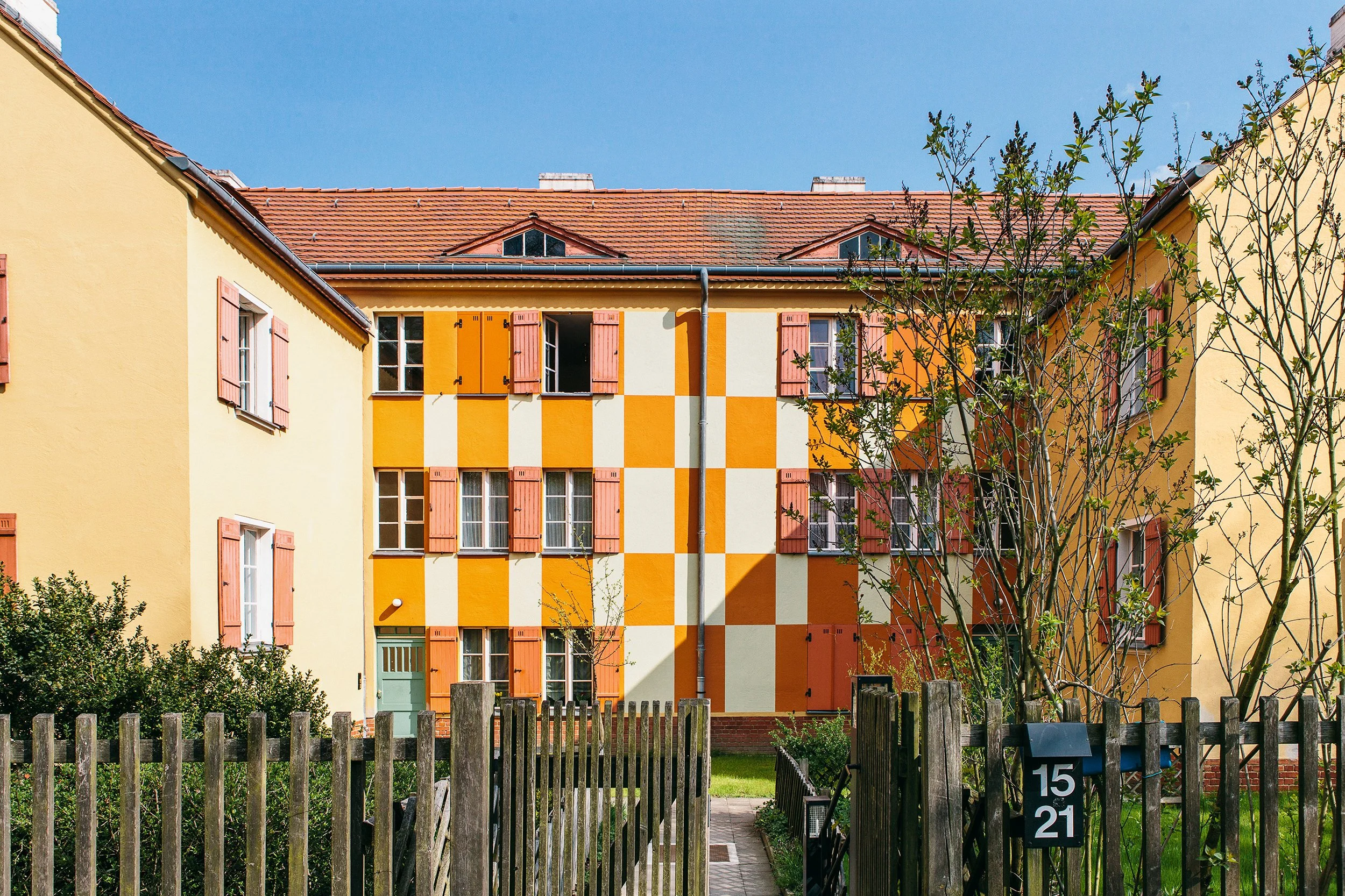Boligfelt i Gartenstadt Falkenberg i Berlin, tegnet av arkitekt Bruno Taut. Gul murbygning med orange sjakkmønster på veggen. Vinduene har rosa vinduslemmer.