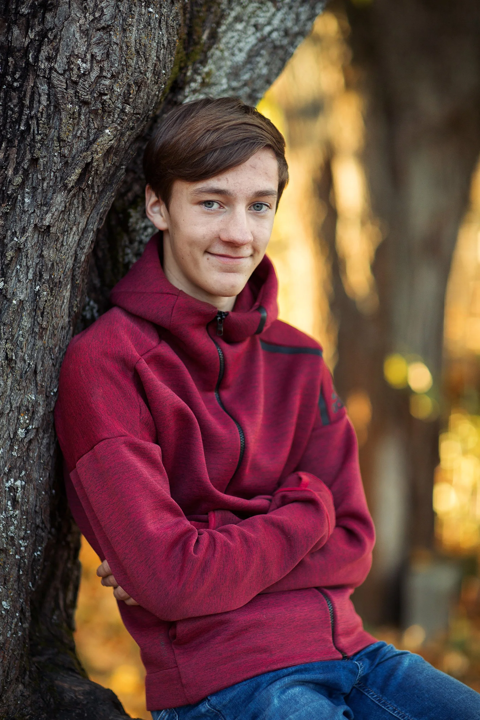 Konfirmantfotografering av gutt sittende i et tre med ryggen lent mot stammen