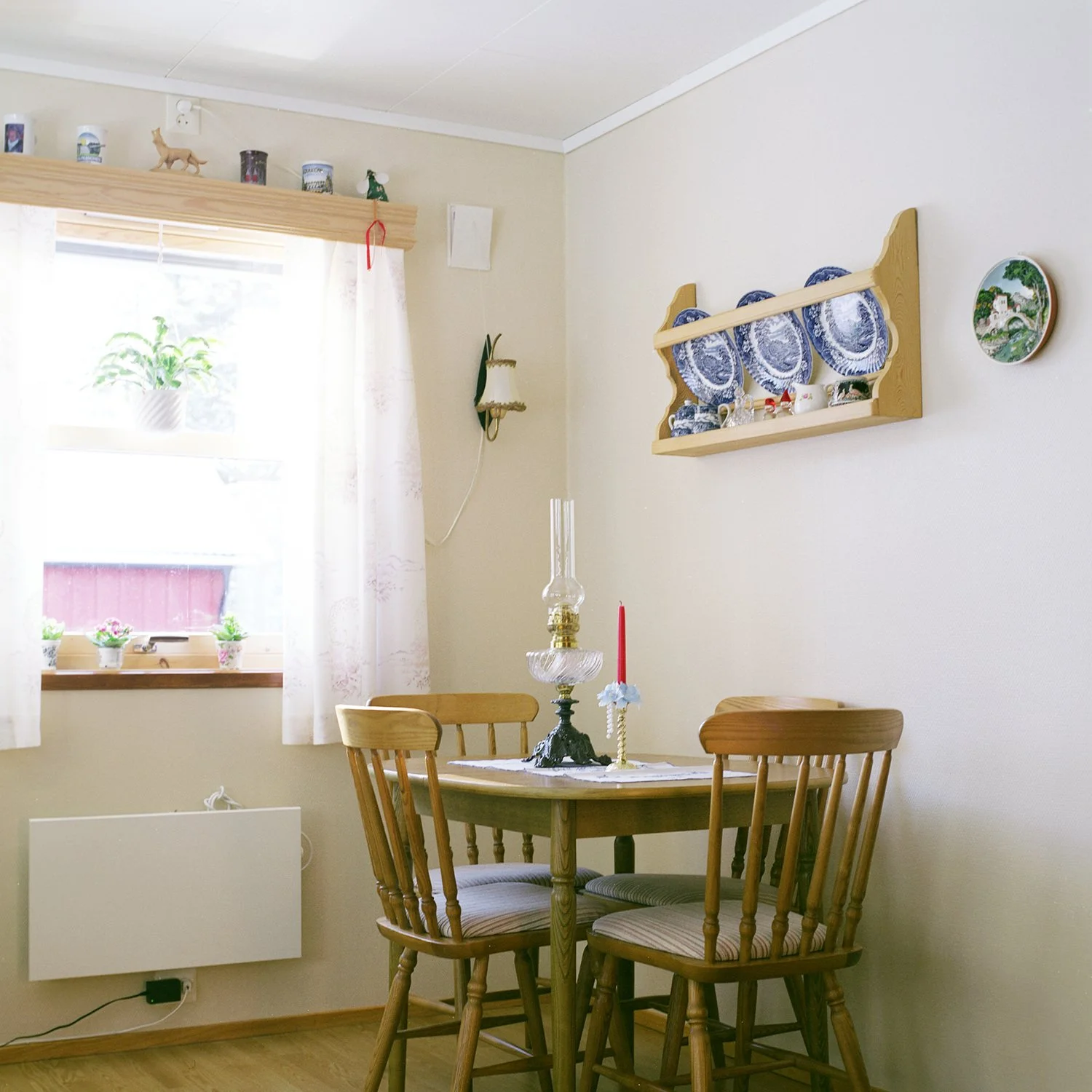 Utsnitt av interiør. Stuekrok med spisebord og fire stoler og tallerkenhylle på veggen.