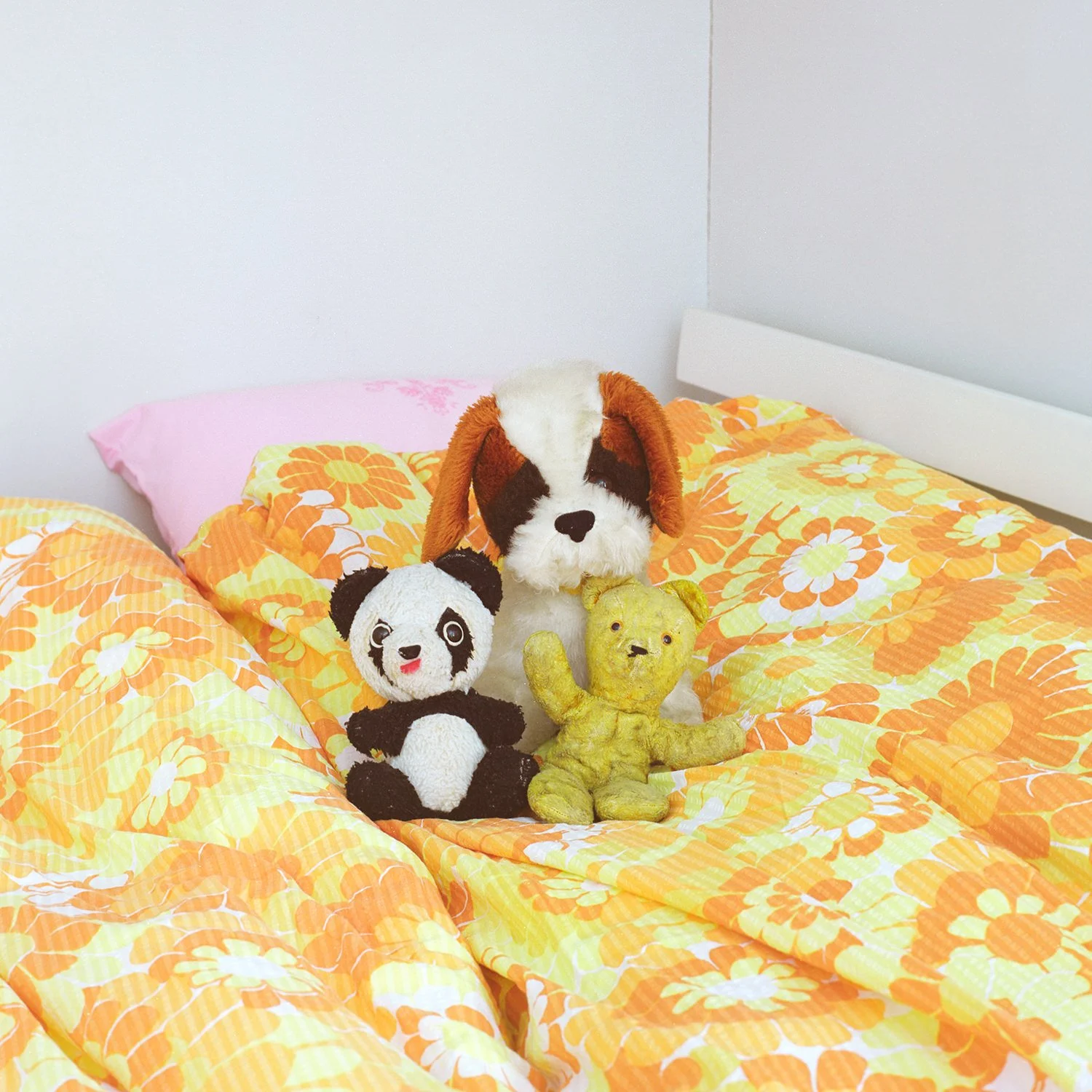 Interiør. Tre kosebamser sitter på et retro sengesett i gule fargetoner.