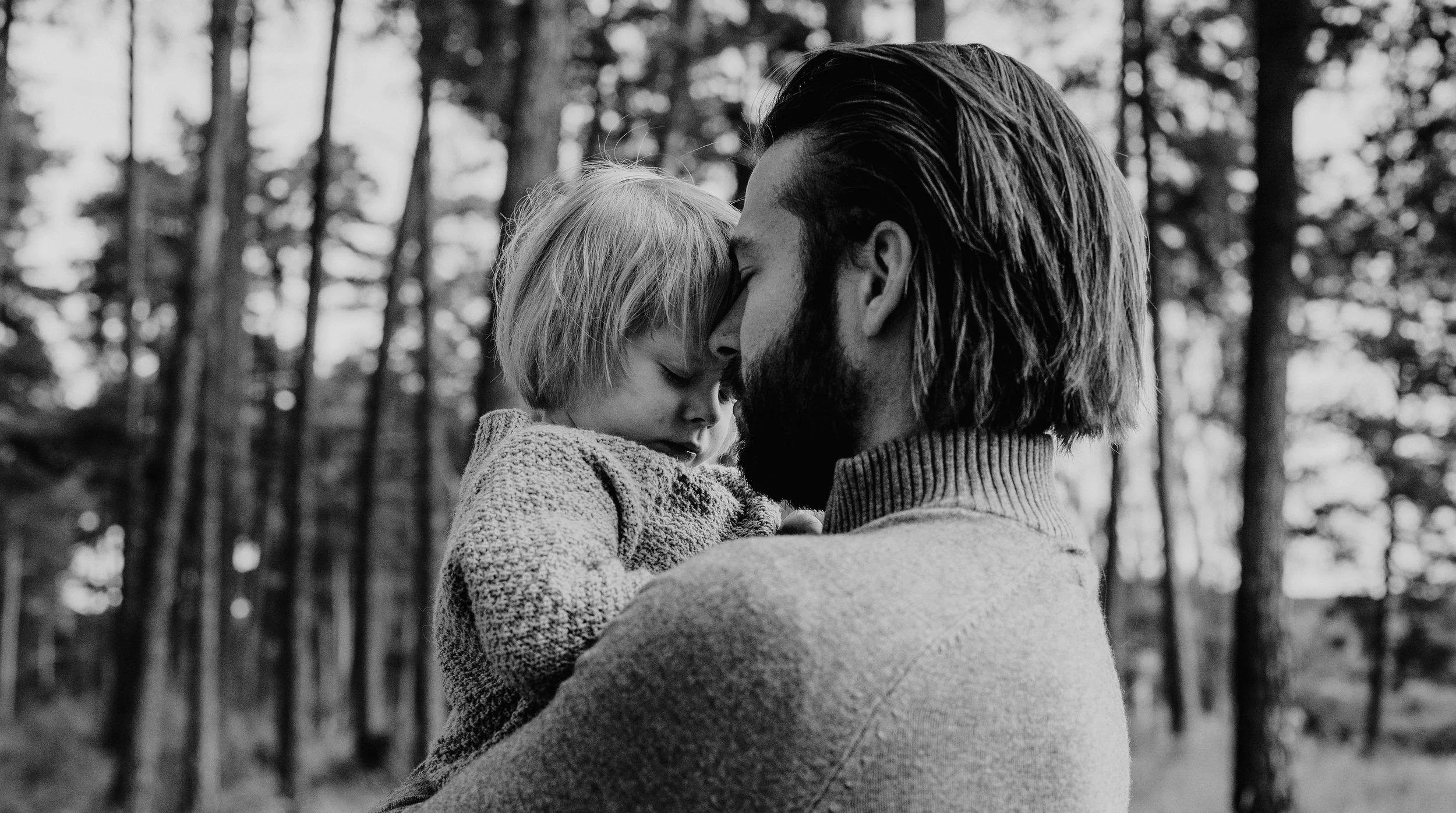 Familiefotografering utendørs i naturlig lys. Pappa holder barnet sitt i armene.