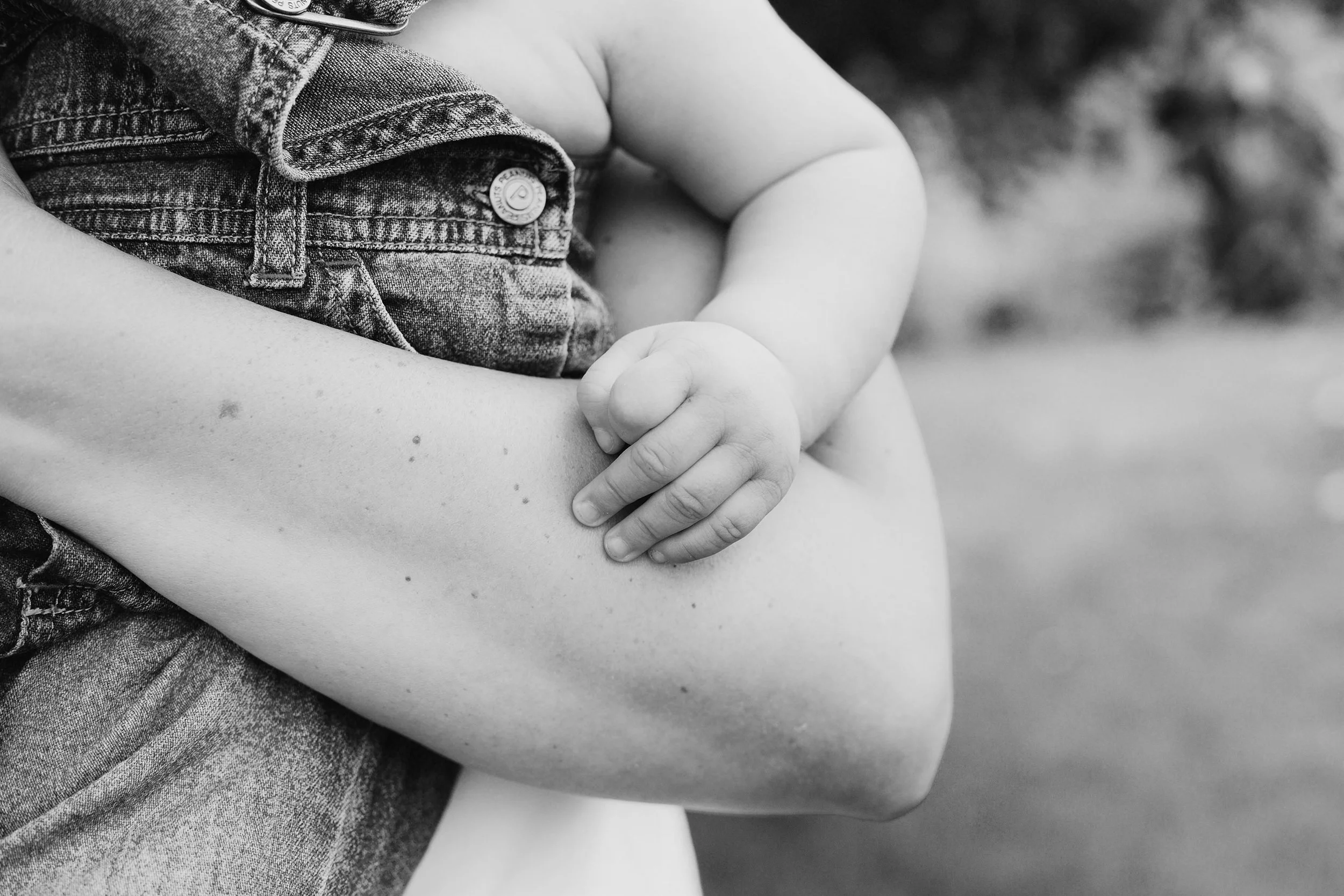 Liten barnehånd holder på mammas arm under familiefotografering.