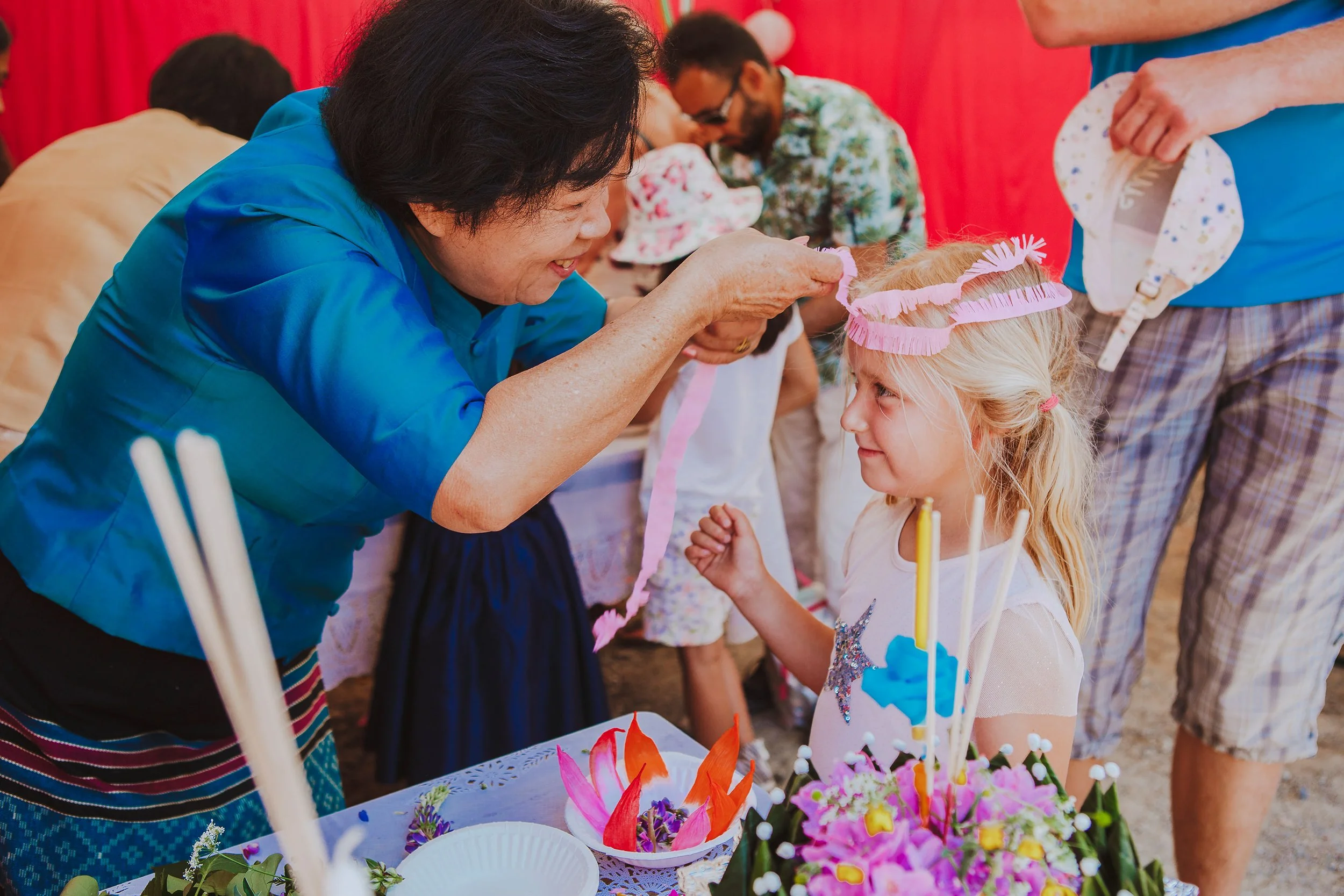 Stoppested Verden internasjonal barnefestival. En voksen kvinne hjelper en liten jente å knyte et pannebånd i papir.