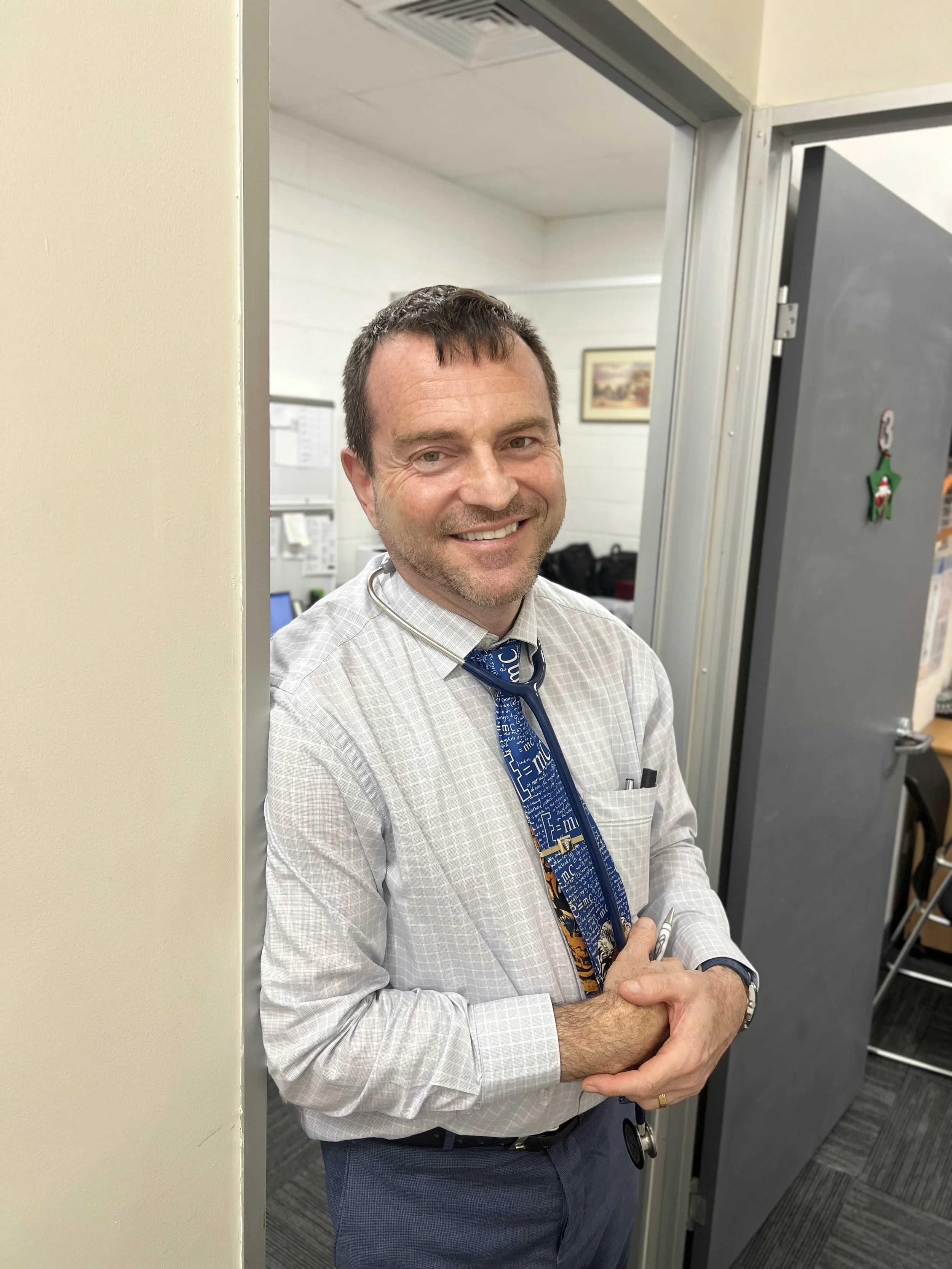 A man with a stethoscope standing in a doorway, smiling at the camera.
