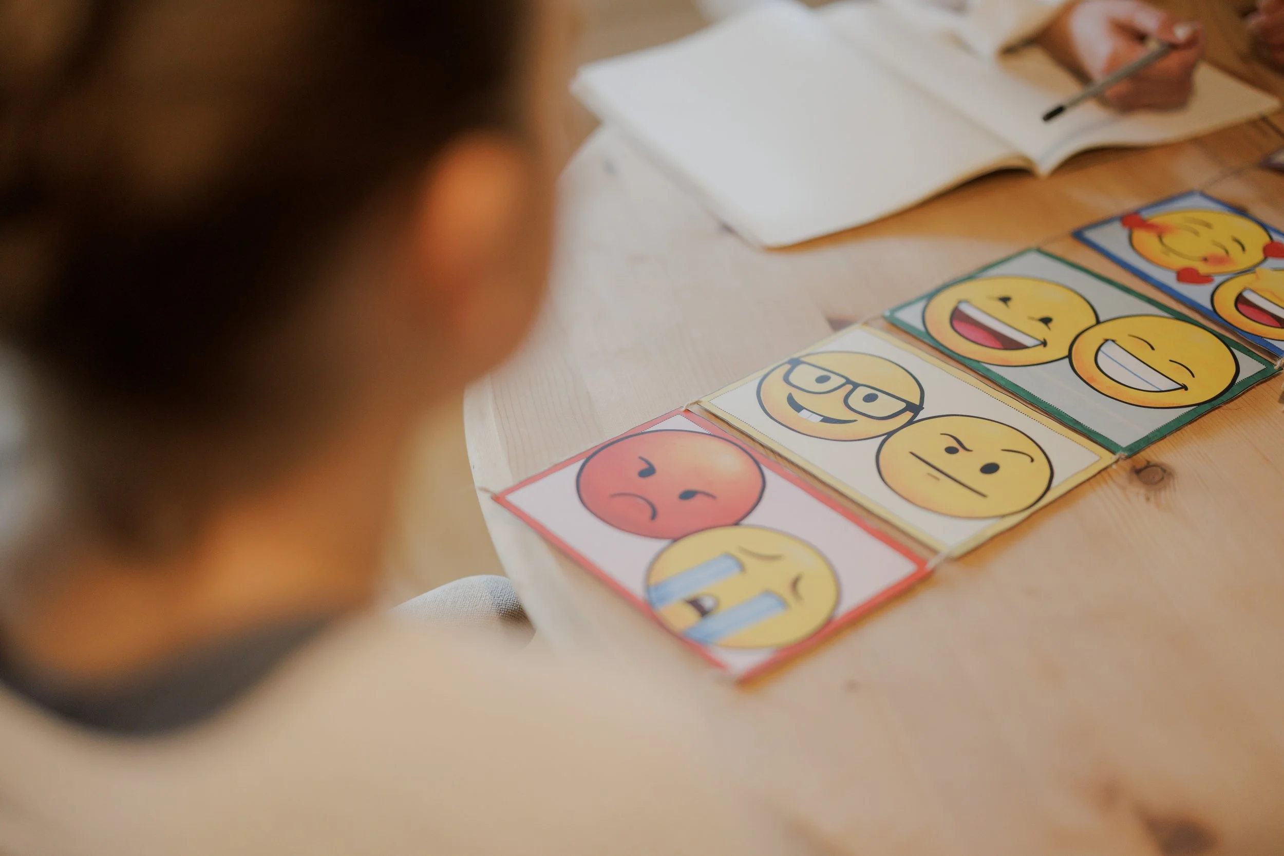 Ein Kind schaut auf eine Tabelle mit verschiedenen lachenden und traurigen Emojis, die auf Papier gedruckt sind.