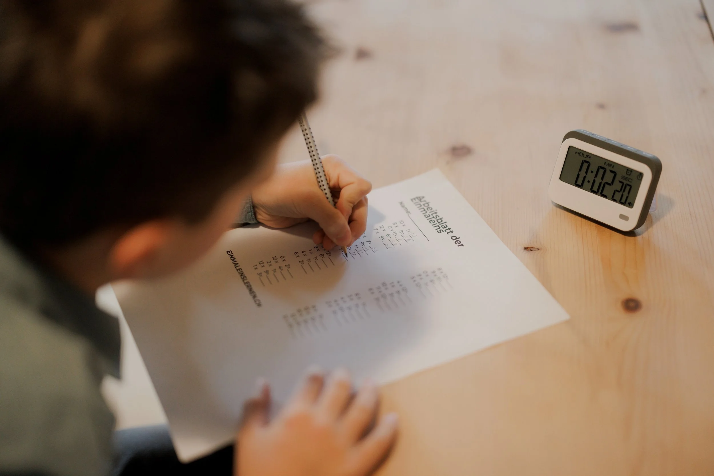 Ein Kind schreibt auf einem Arbeitsblatt zur Tierpflege auf einem Holztisch, während eine digitale Stoppuhr auf dem Tisch läuft.