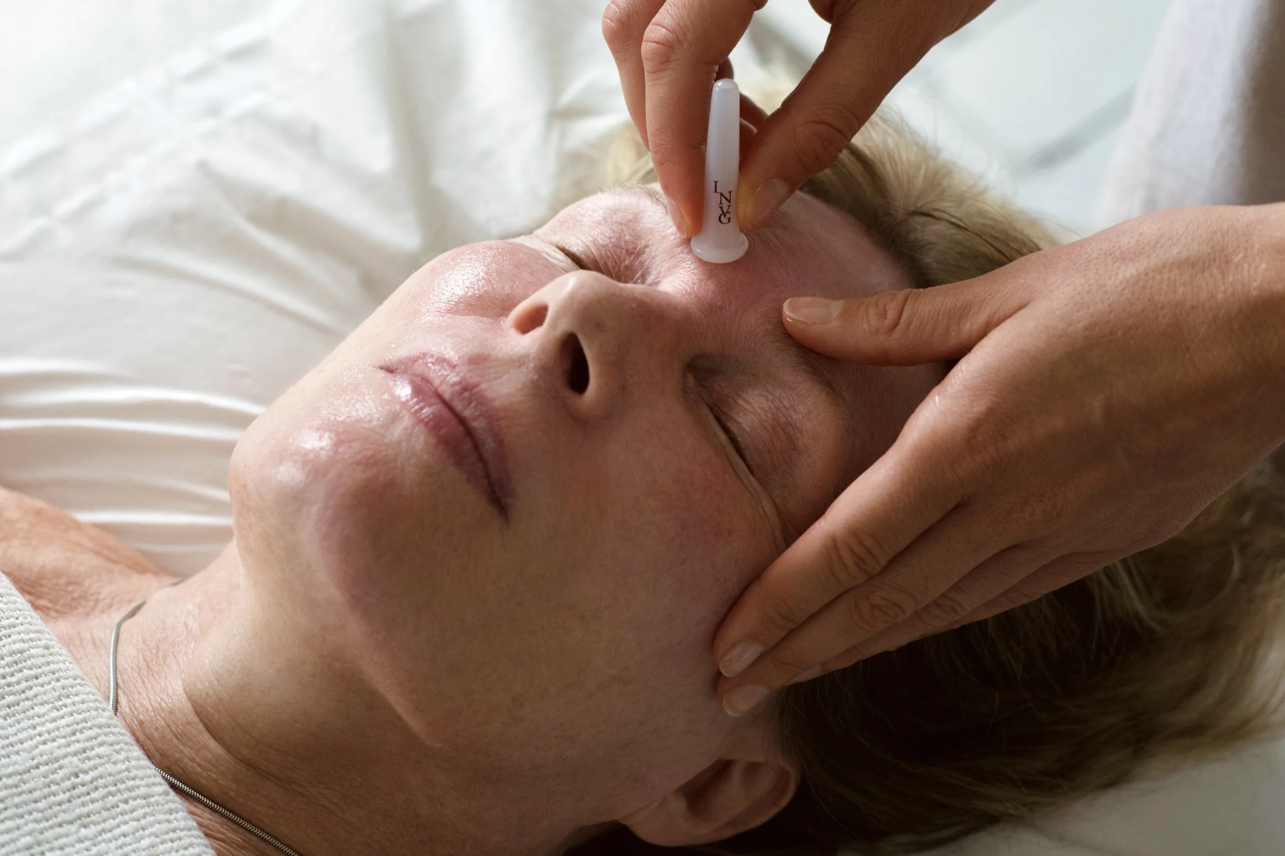 A person receiving a facial treatment with a skincare professional applying a treatment on their forehead using a small applicator.