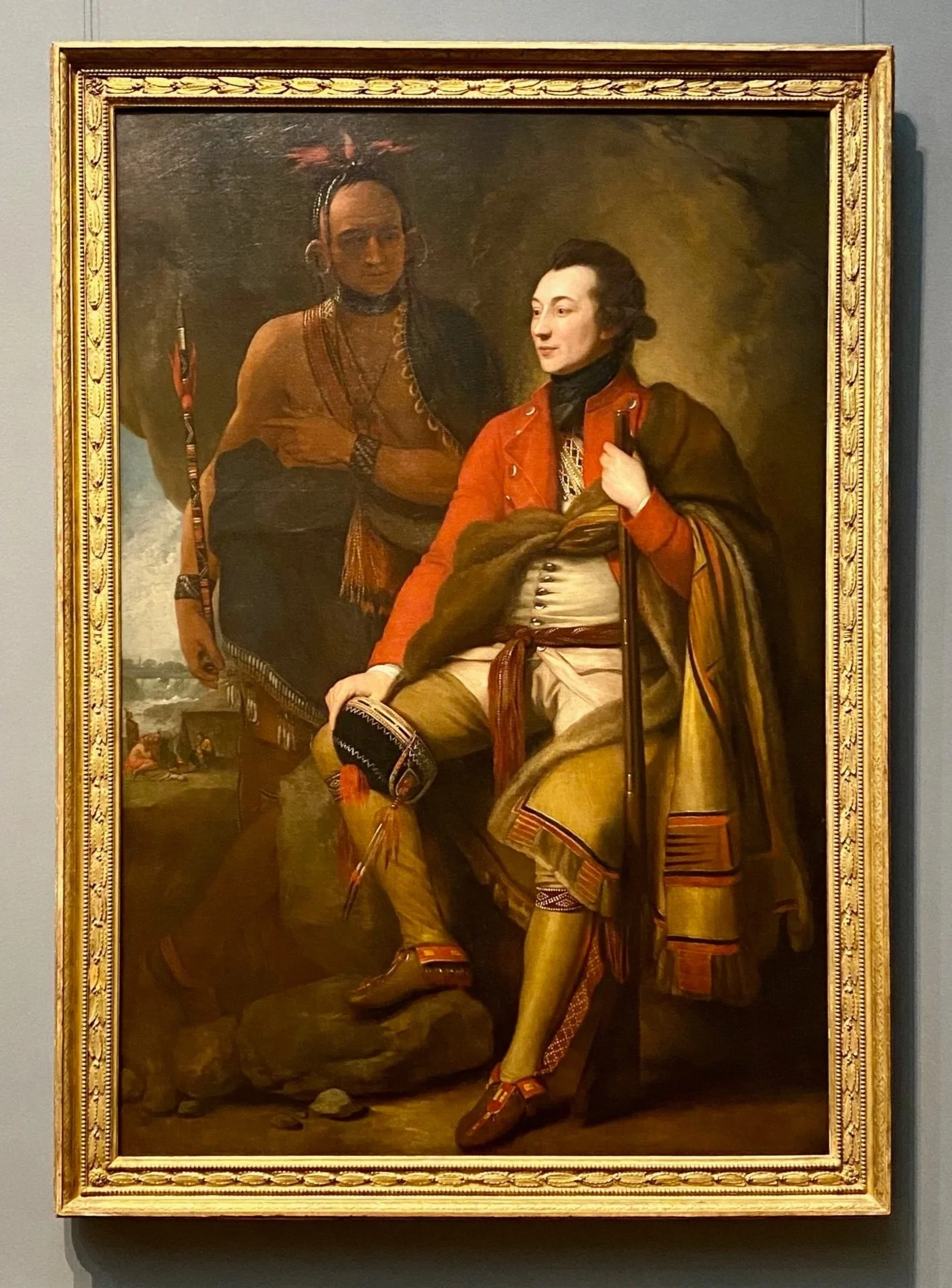 This is a painting titled "Colonel Guy Johnson and Karonghyontye (Captain David Hill)" by the American painter Benjamin West.  A painting of two men in period clothing, with one standing and one seated, inside a frame.