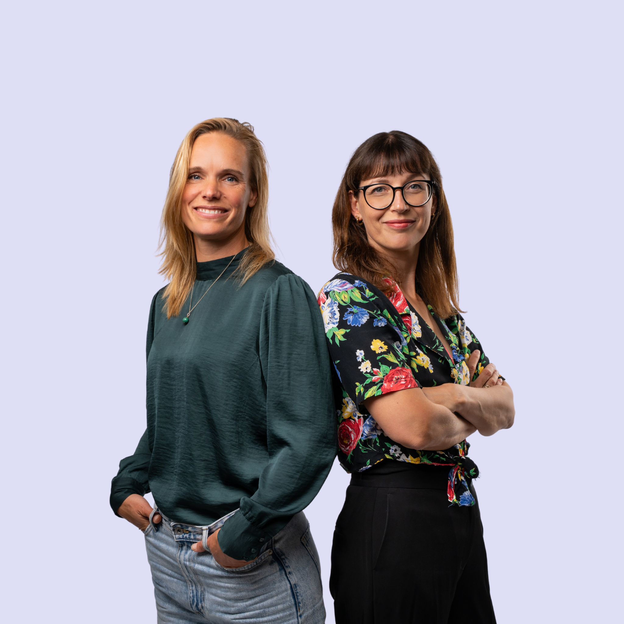Lyke en Laura samen,  staand naast elkaar tegen een lichtpaarse achtergrond, beide glimlachend en in een relaxte houding.
