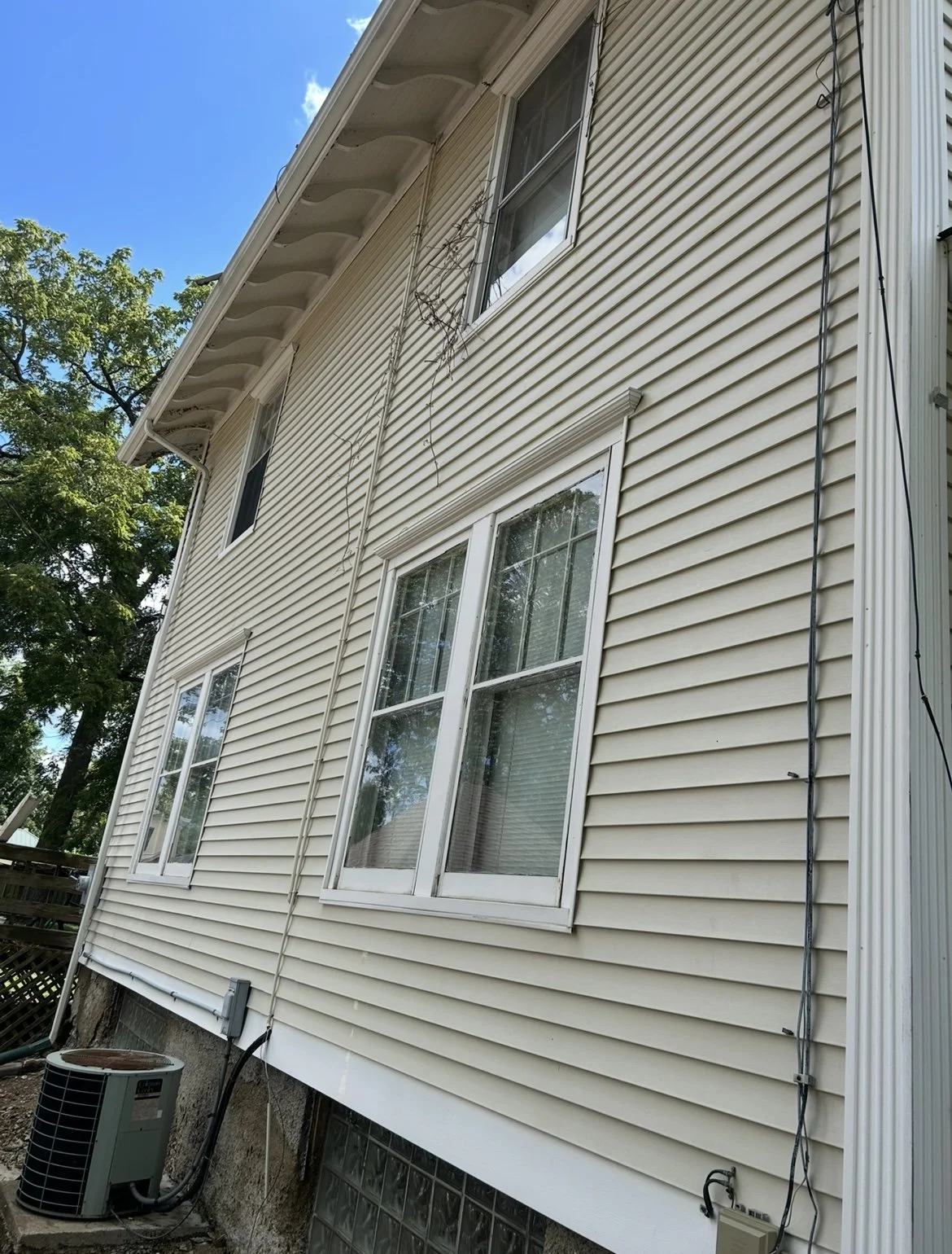 Side view of a beige house with vinyl siding, four windows, and outdoor air conditioning unit.