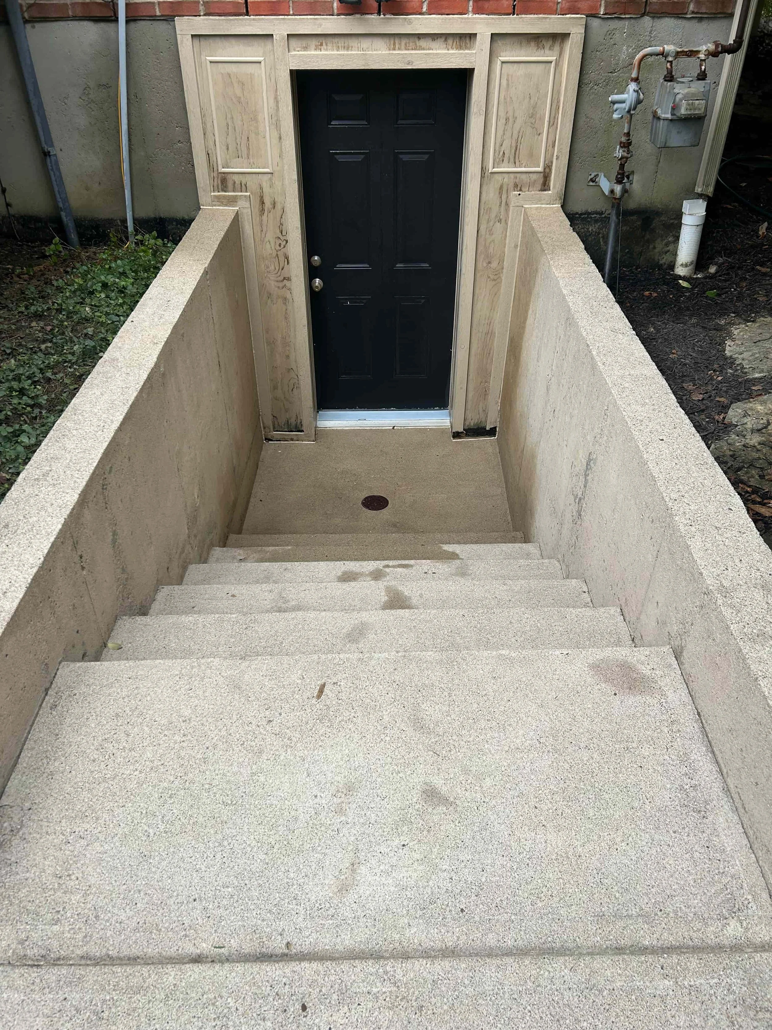 Concrete stairs leading to a door at an underground entrance, with concrete walls on either side, and a black door at the top.