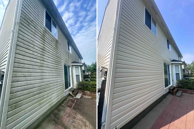 Side of a house with yellow vinyl siding, brick foundation, and lush green bushes in front, under a clear blue sky.
