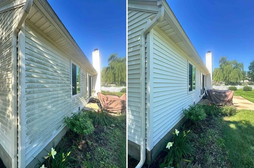 Side-by-side comparison of a house exterior with before and after cleaning. Left side shows weathered, dirty white siding, right side shows clean, bright siding. Garden with lilies is visible in front, blue sky overhead.