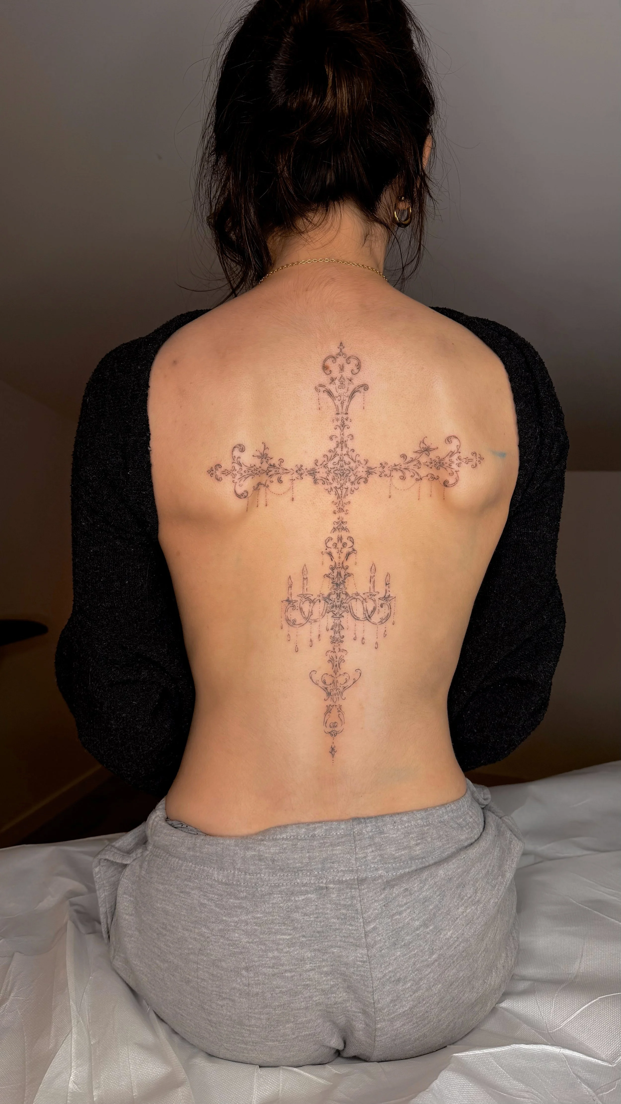 Tatouage d'une grande croix élégante et détaillée dans le dos d'une femme, avec des chandeliers et des éléments décoratifs gothiques.