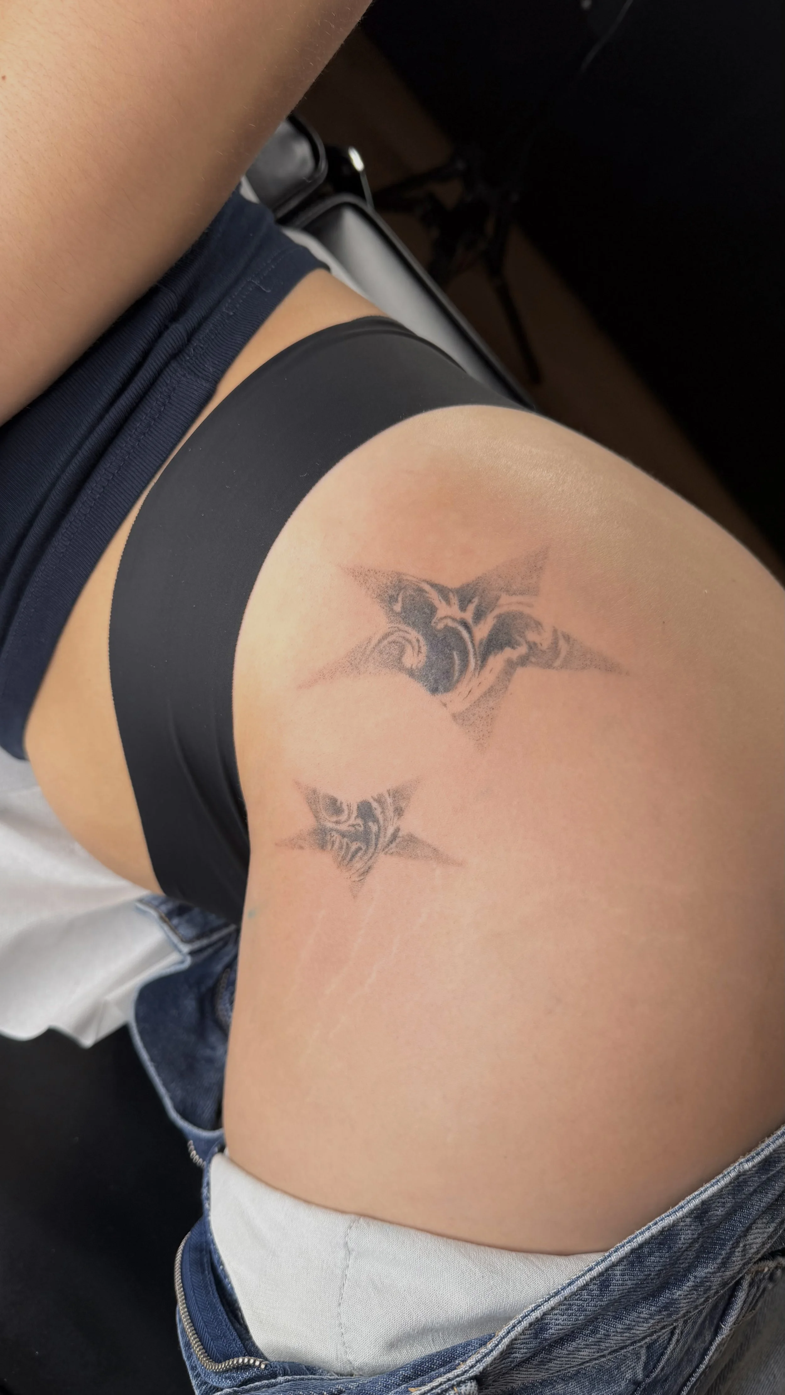 Une personne portant un costume de bain noir avec une robe en jean. Elle a un tatouage de deux chauves-souris sur la cuisse gauche.
