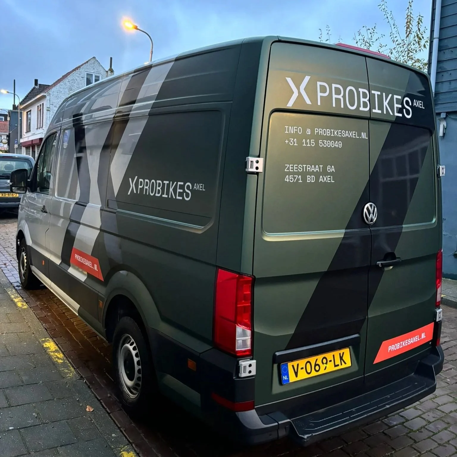 Een groene bedrijfswagen met reclame voor PROBIKES AXEL, inclusief contactgegevens en website, geparkeerd op straat.