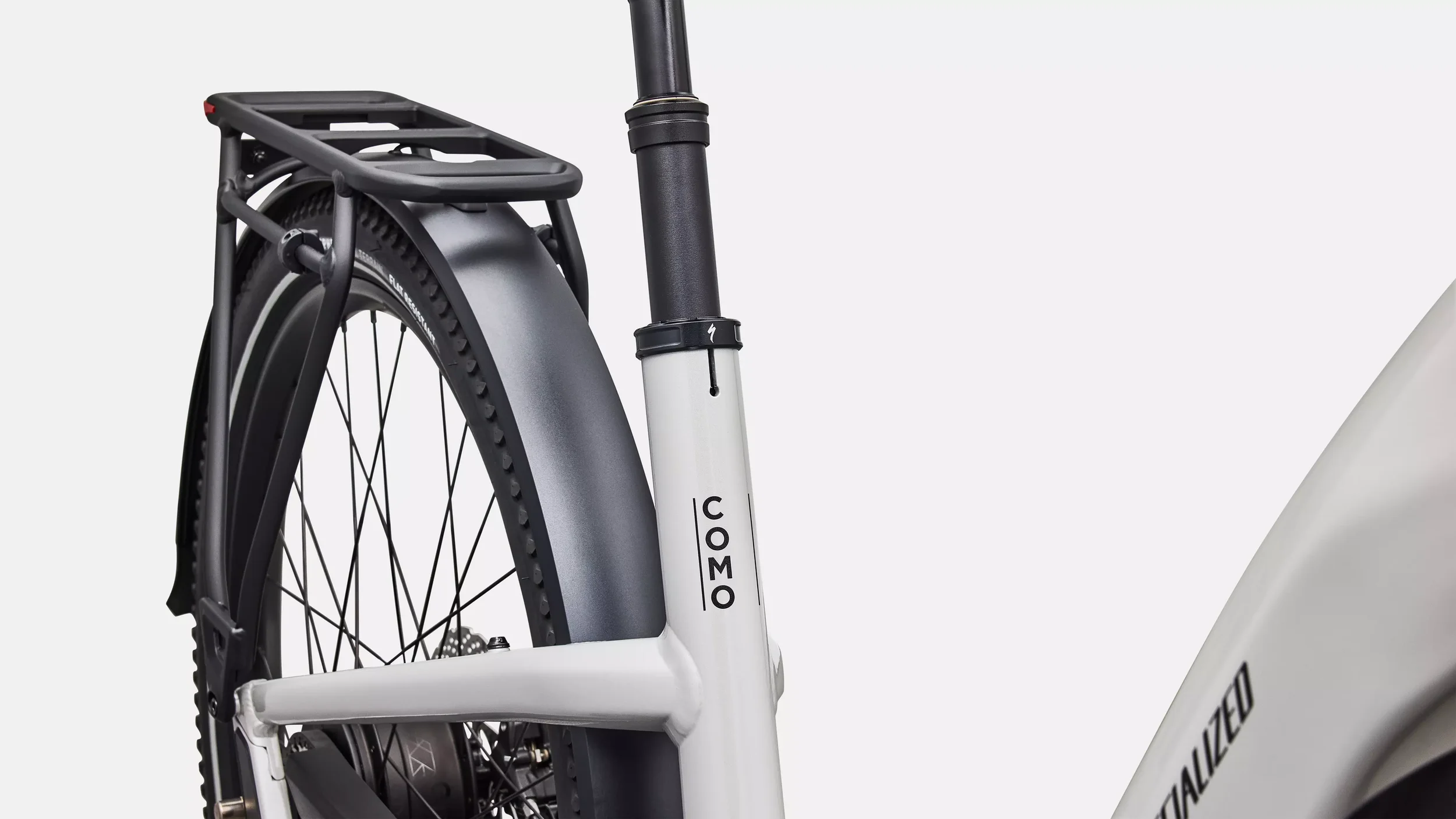 Close-up van een lichtgrijze elektrische Specialized fiets met zwart zadel en zwart stuur, met de letters 'COMO' op de framebuisklep.