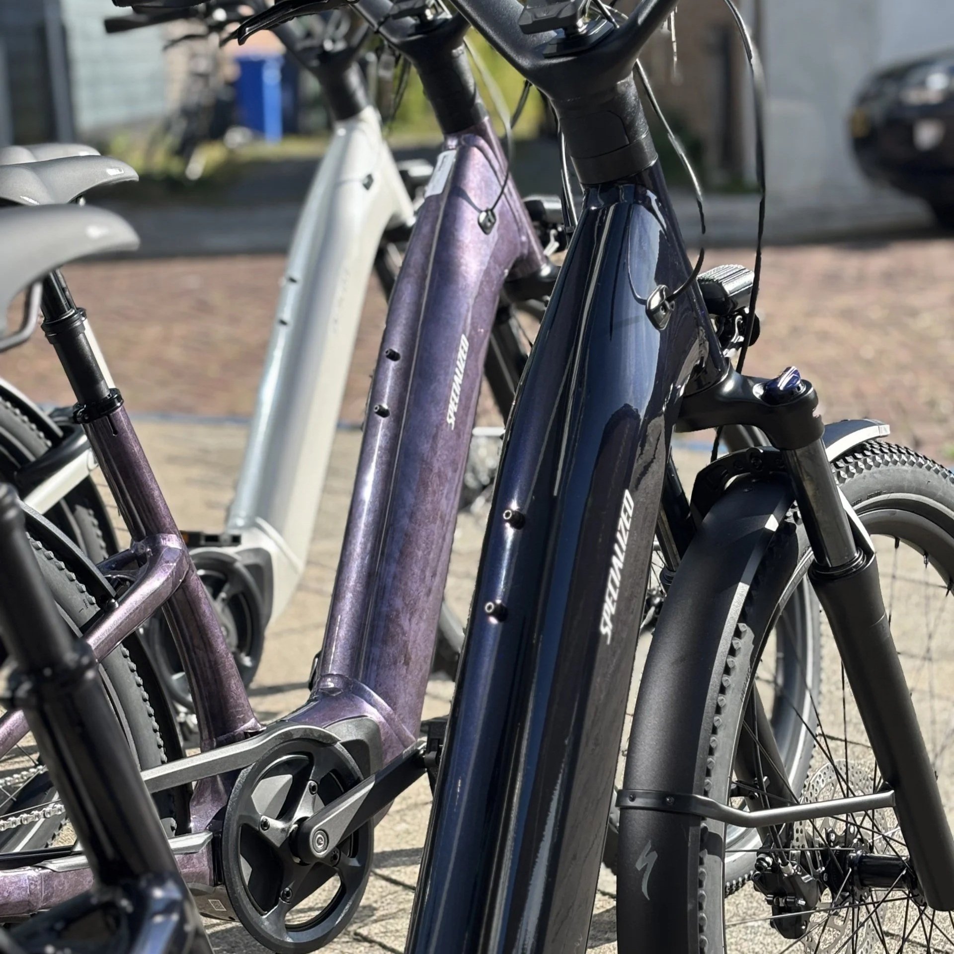Drie elektrische Specialized COMO 4.0 NB staan naast elkaar op een straat, met de focus op de frames en voorvorken.
