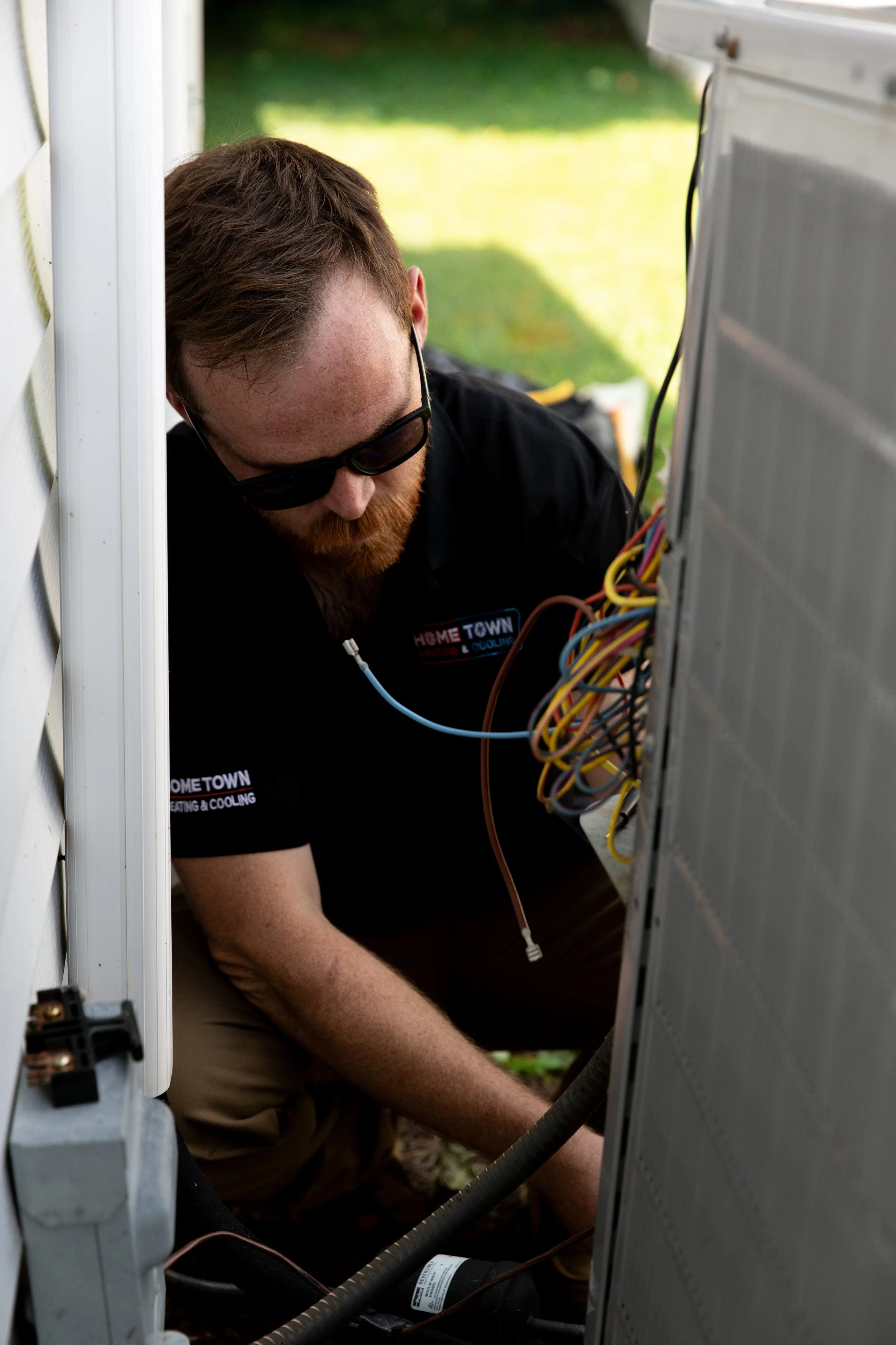 Technician working on outdoor HVAC system wiring near the house