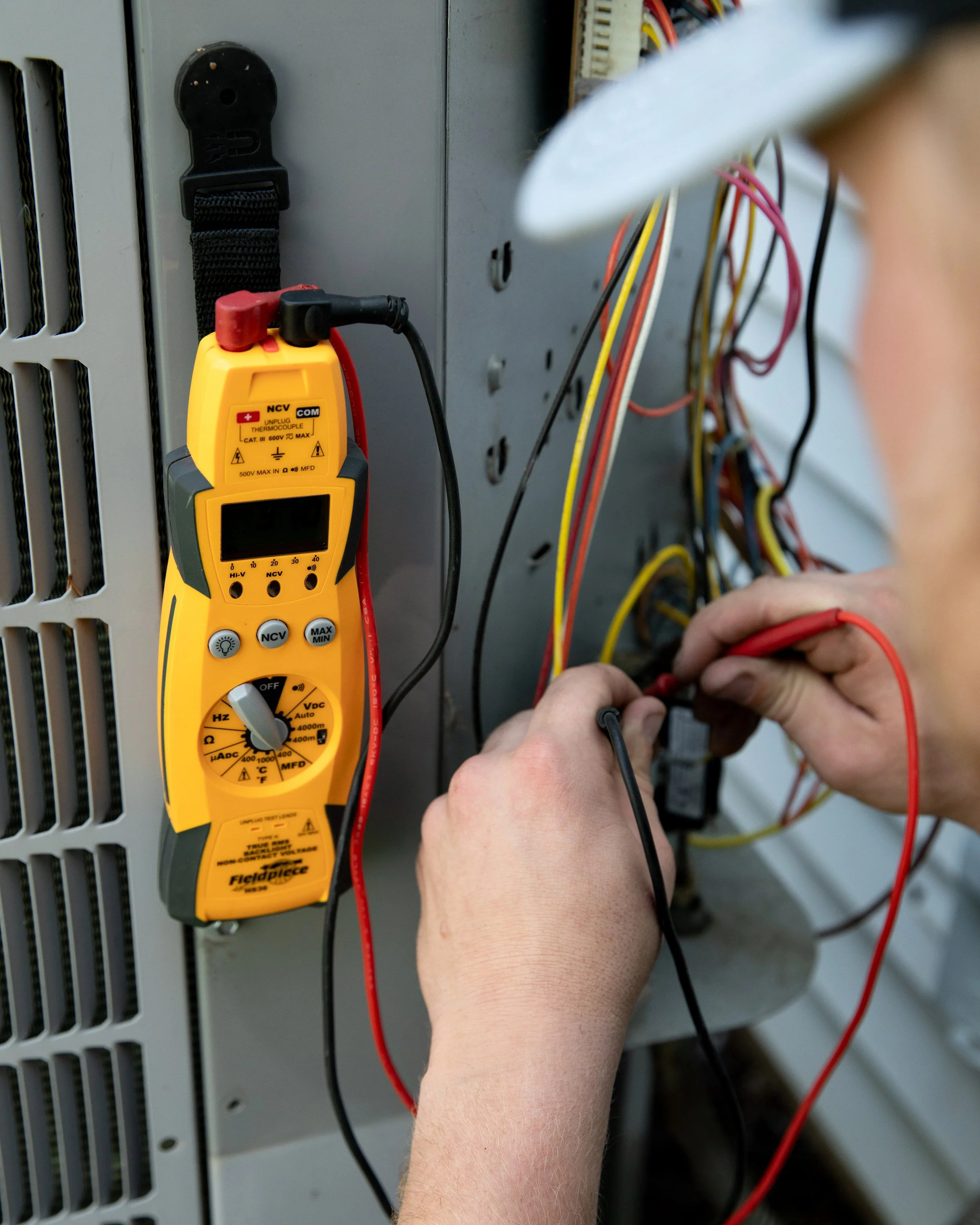 A person using a multimeter to test wiring inside an electrical panel.