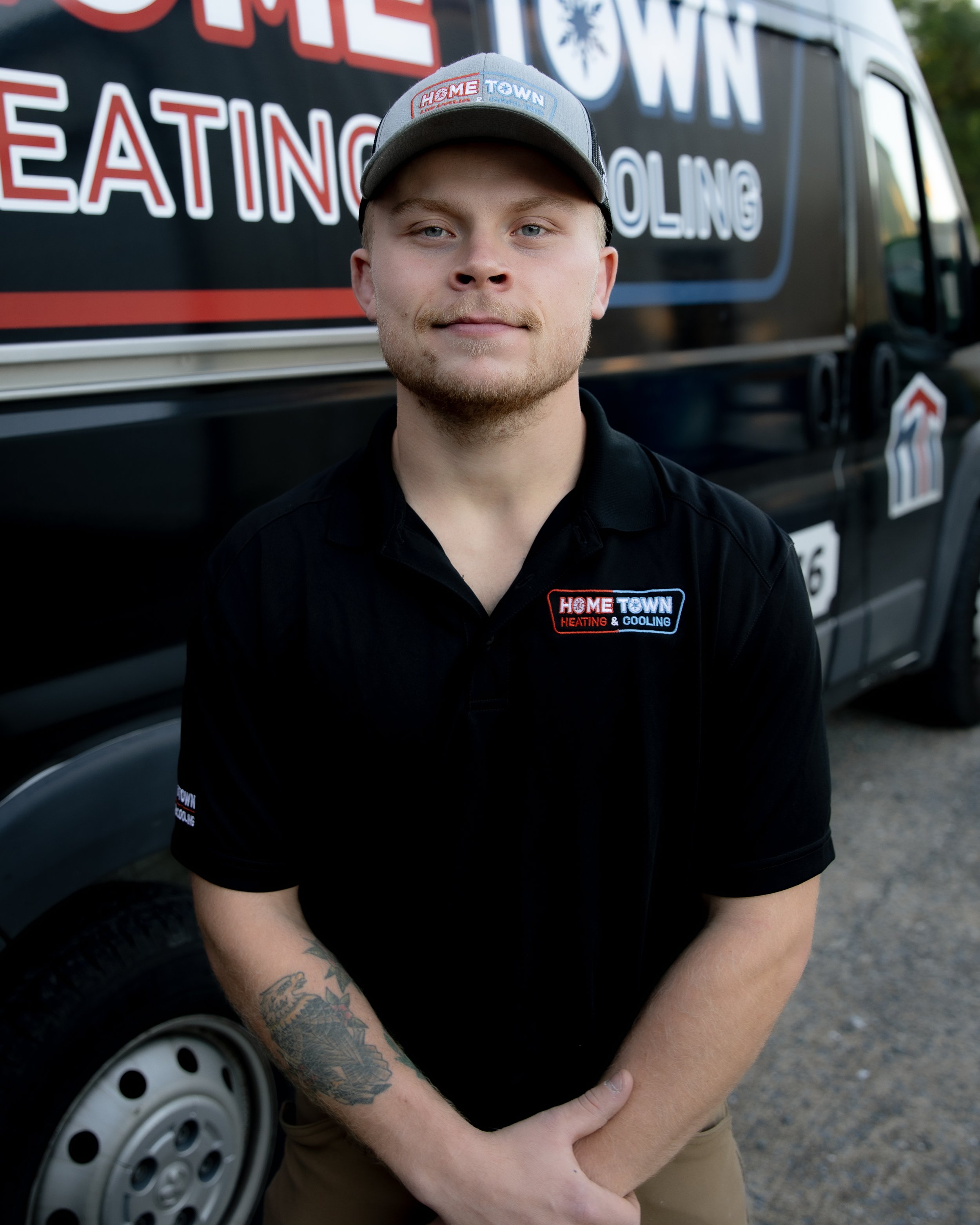 A man in uniform standing in front of a black service vehicle with the logo 'Home Town Heating & Cooling'.