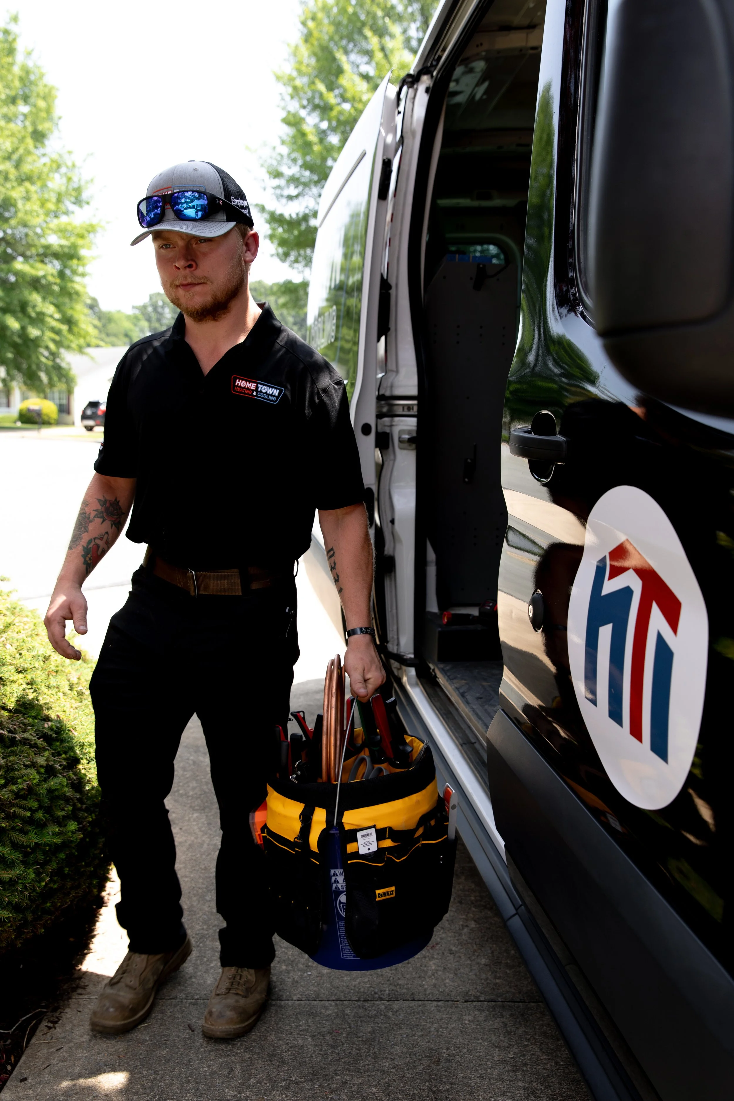 A handyman holding a toolbox containing tools standing next to a business vehicle, outdoors on a residential street.