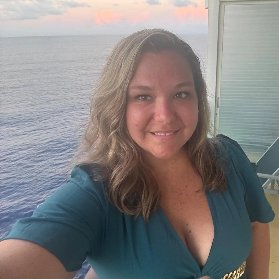 A woman taking a selfie on a balcony overlooking an ocean at sunset.
