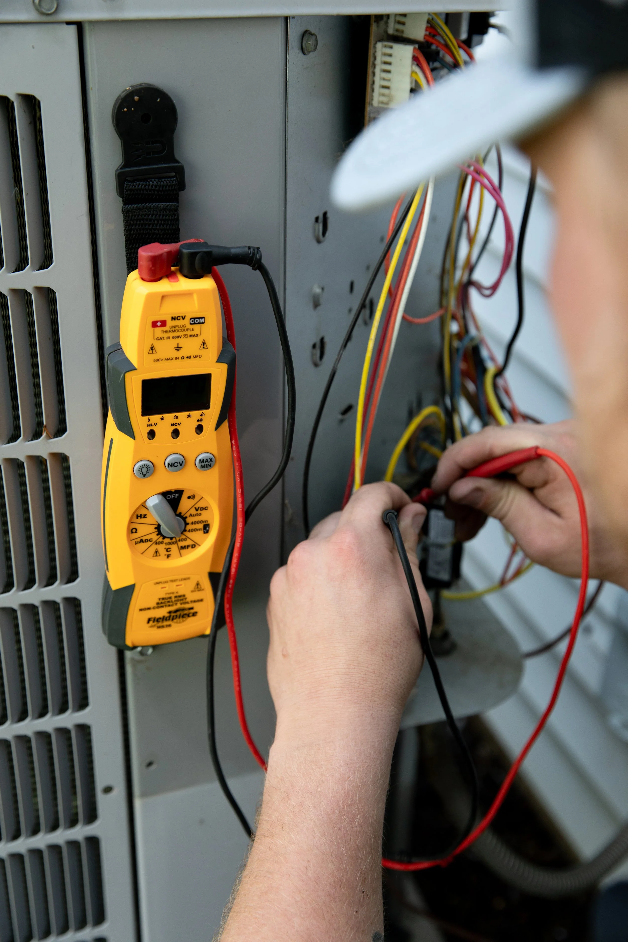 A technician is using a multimeter to test electrical wires inside an HVAC system.