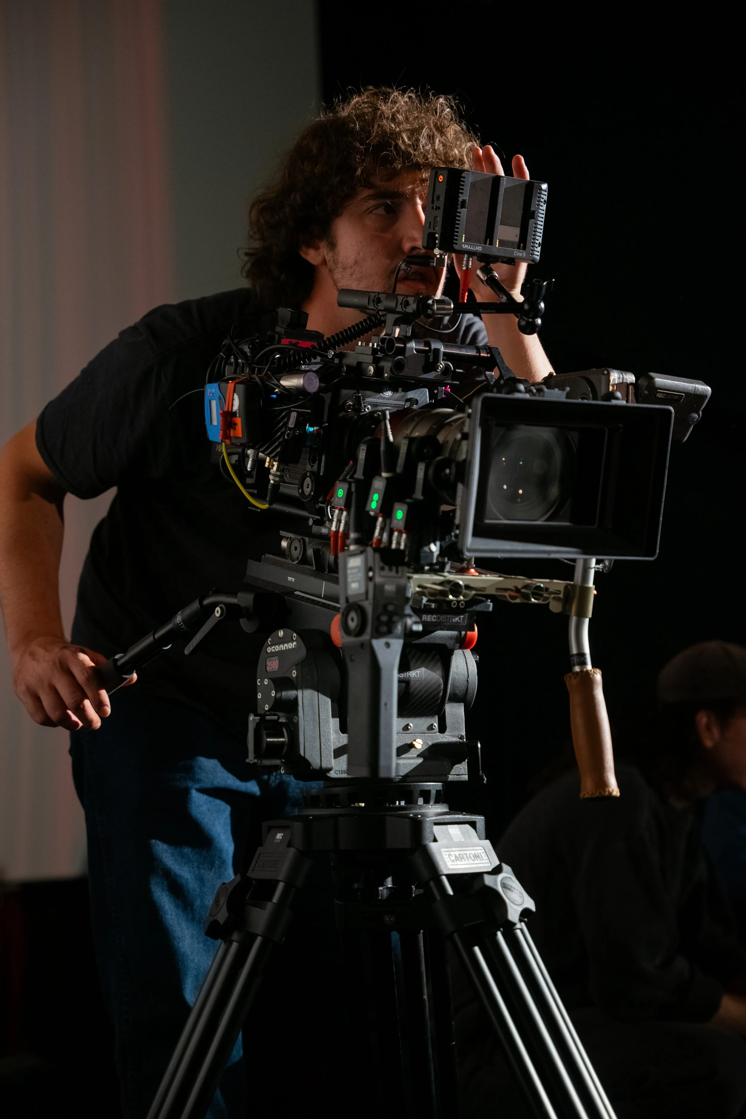 A person operating a professional film camera on a tripod, adjusting the viewfinder during a shoot.