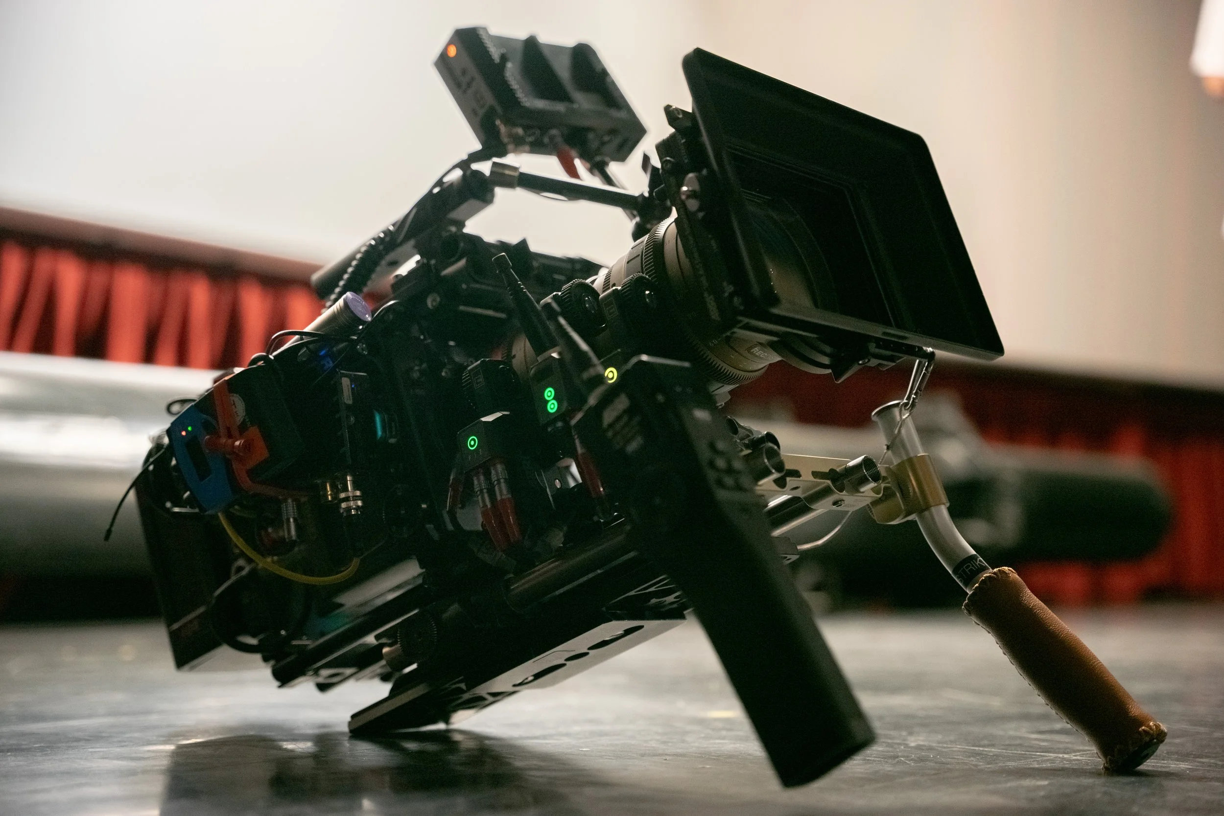 Close-up of a professional camera mounted on a steady support, positioned on a flat surface with a roller handle, in a dimly lit setting.