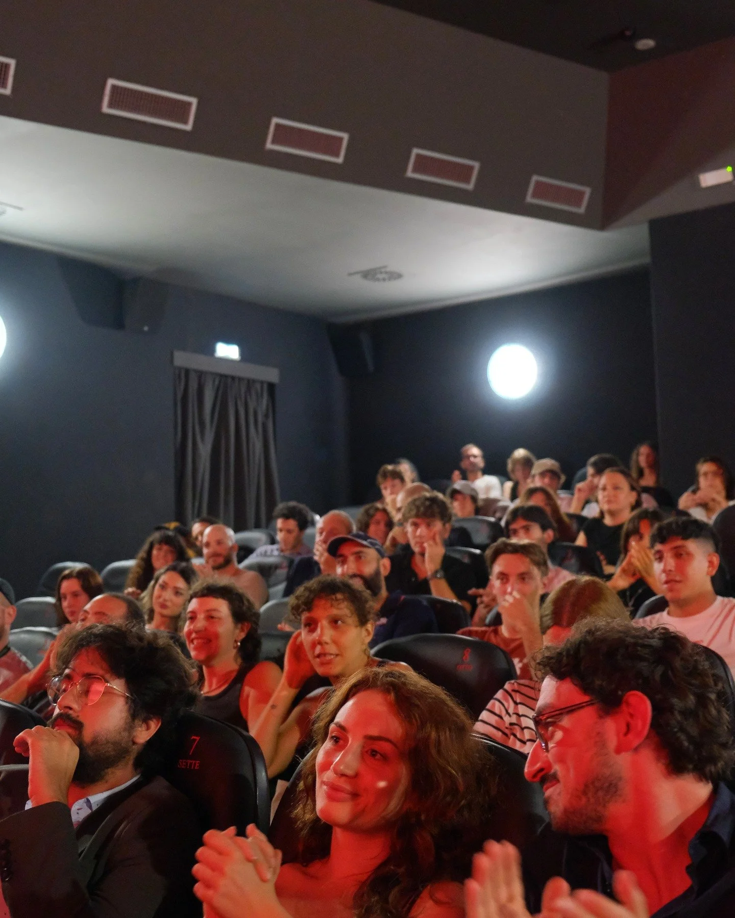 People sitting in a movie theater, some clapping, watching a film or presentation.