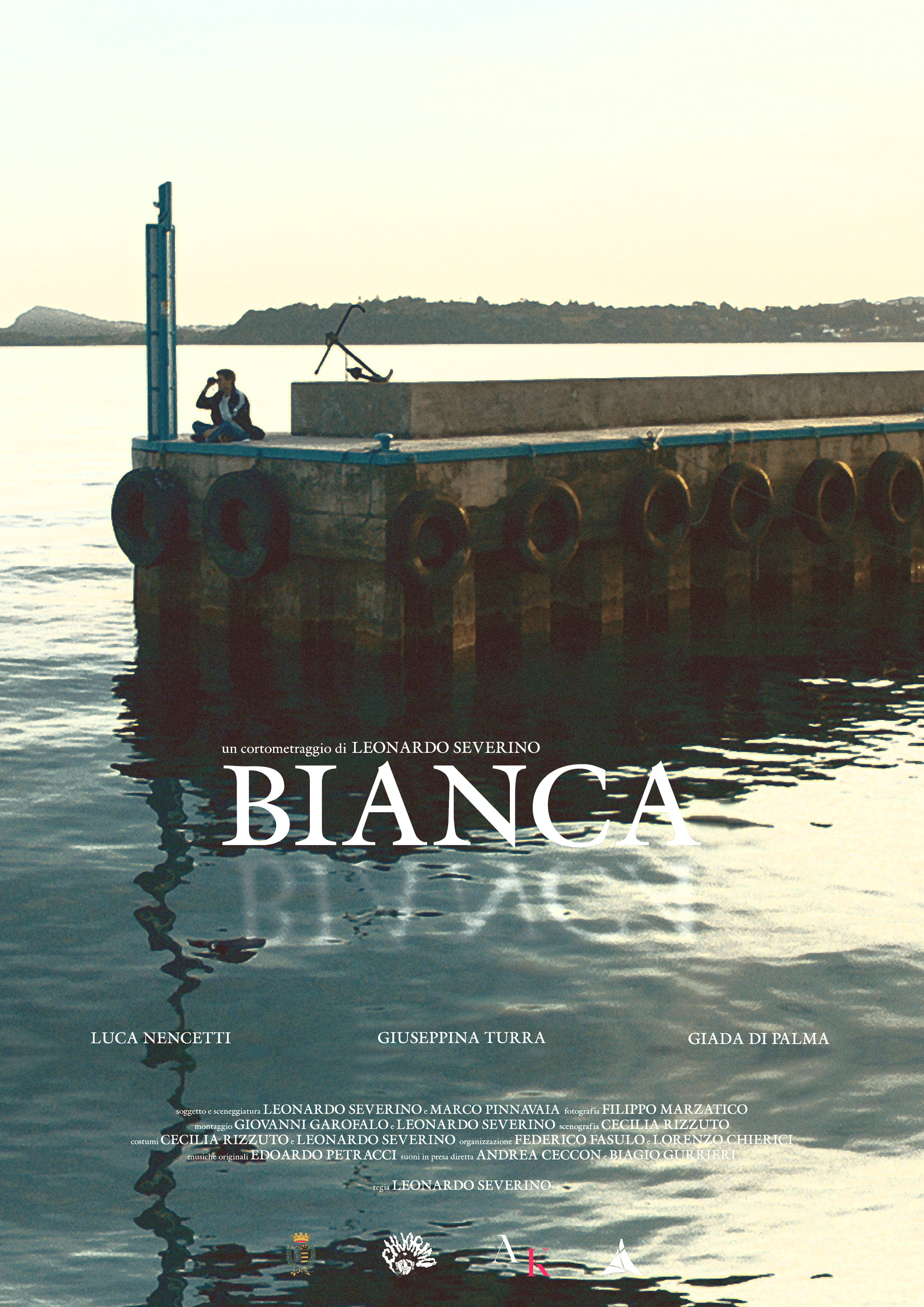 A person sitting on a concrete pier with a bicycle, overlooking calm water at sunset or sunrise, with distant land and hills in the background.