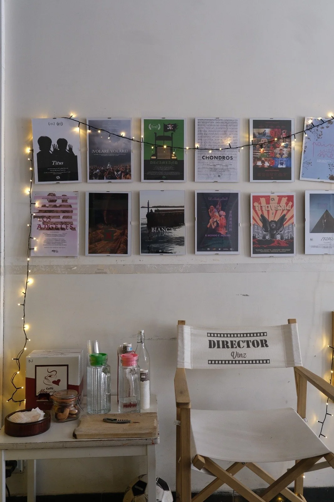 A wall decorated with posters, fairy lights, and a director's chair, along with a small table holding drinks and snacks.