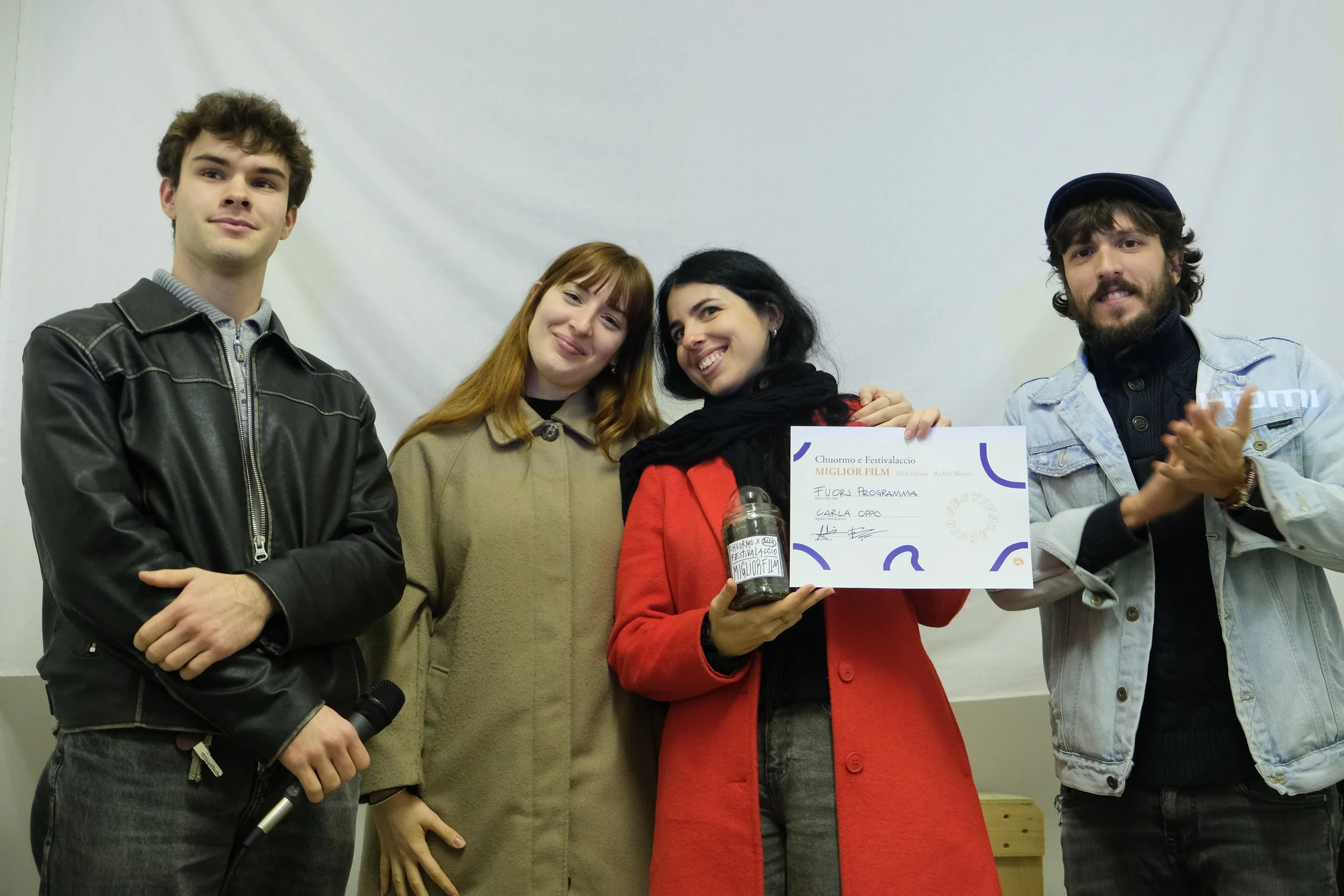 Group of four people, with one woman holding a certificate and a jar, standing against a white background.
