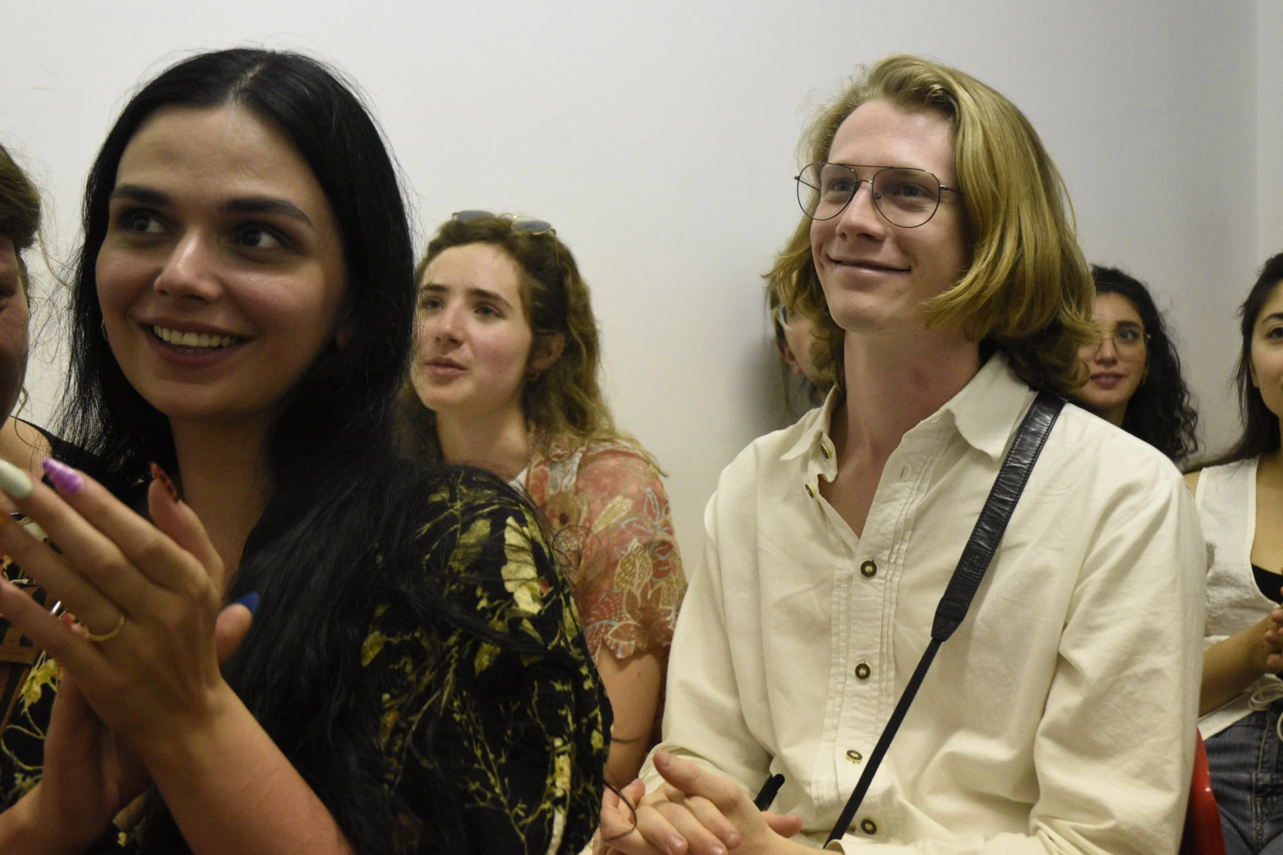 Group of young adults sitting and listening attentively in a room, with diverse facial expressions and casual attire.
