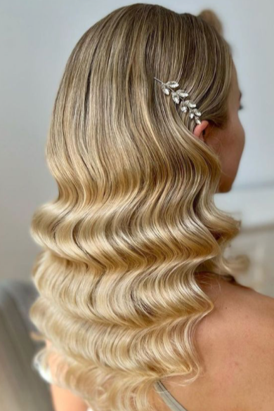 Side view of a woman with long, wavy blonde hair and a decorative hair accessory with leaves and small stones.